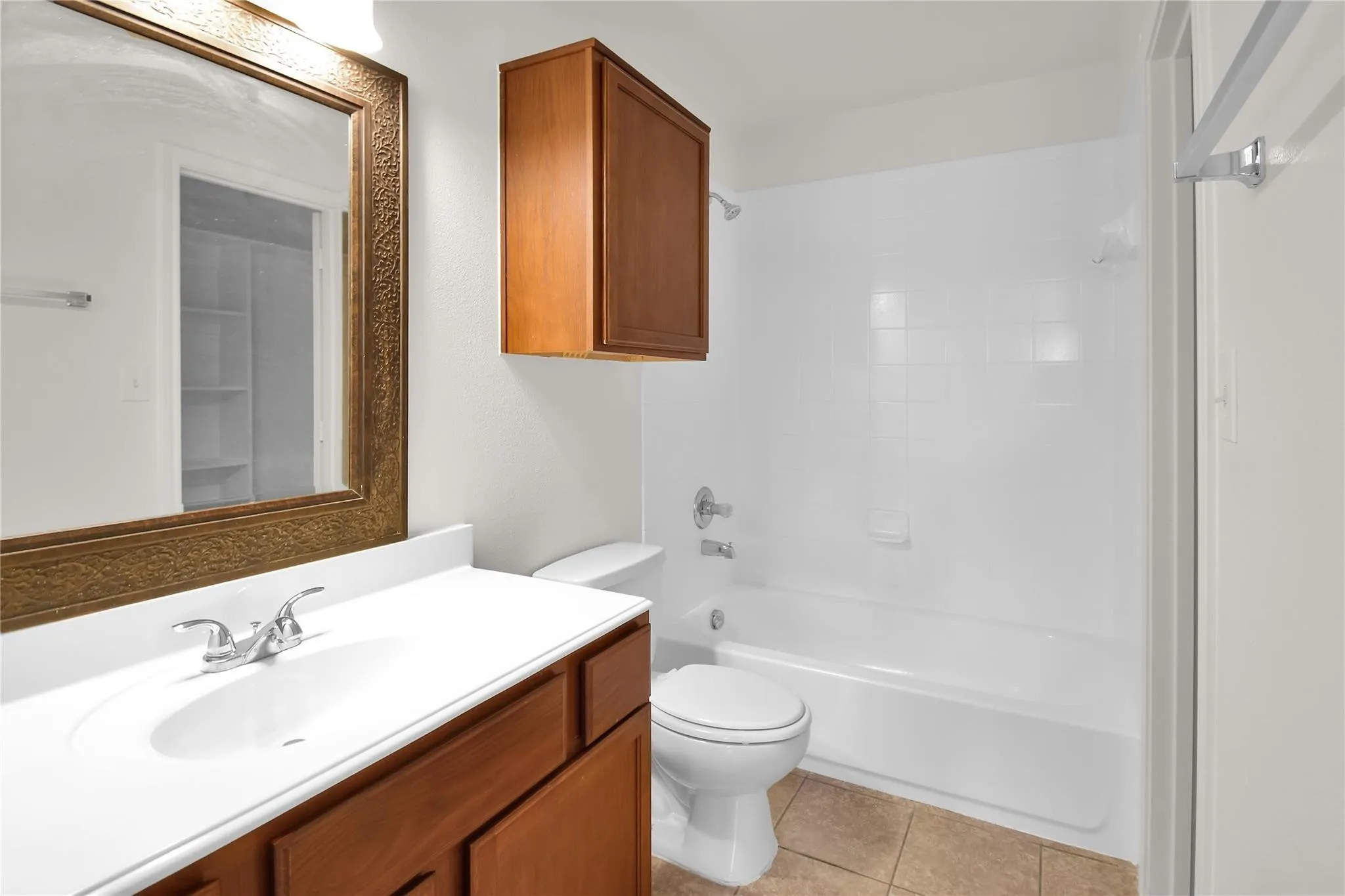 Bathroom featuring a vanity with a white countertop and wood-finish cabinetry, an ornate framed mirror, a built-in medicine cabinet, a toilet, and a white tub with integrated shower
