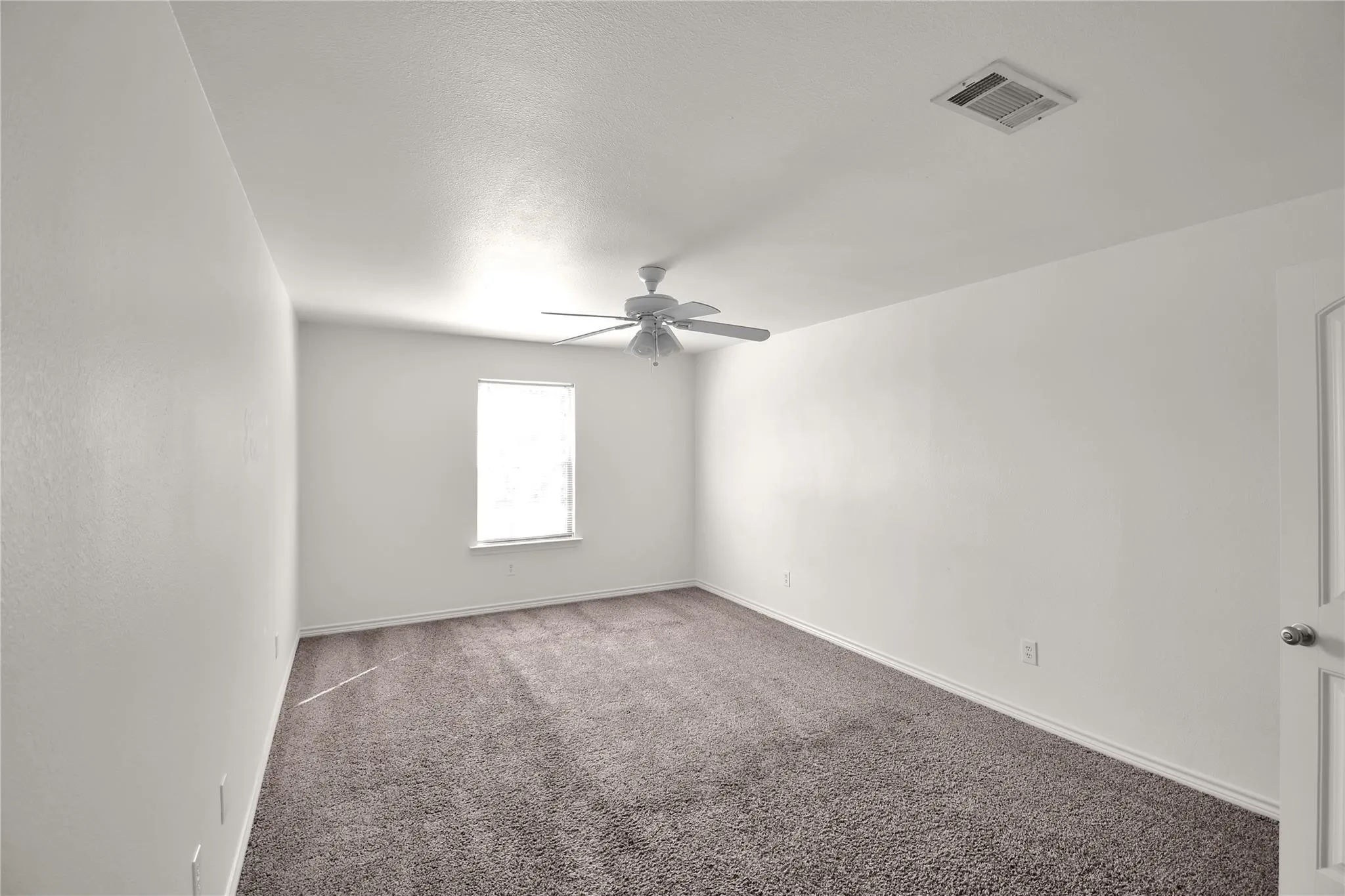 White painted walls, neutral carpet, single window, white ceiling fan, and white paneled door