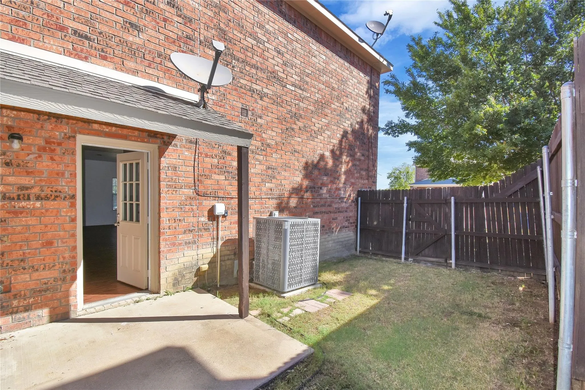 Brick exterior with a covered patio, solid wood privacy fencing, and a grassy area