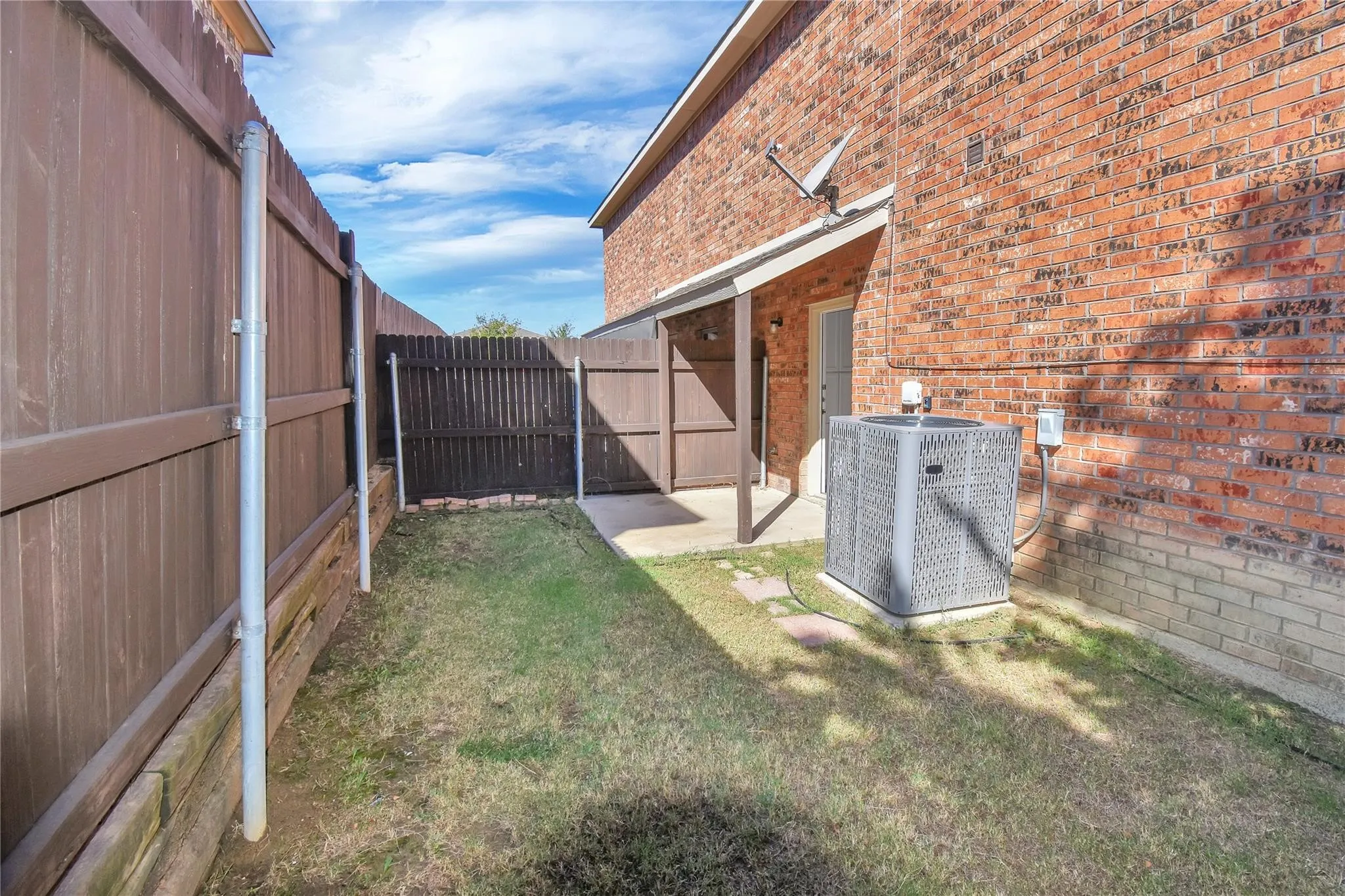 Red brick exterior with an attached patio, privacy fencing, and a grassy area