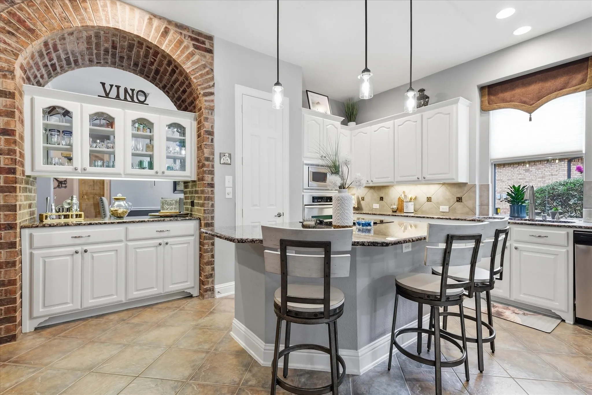 The heart of the home blends function with unforgettable character — a spacious granite island, crisp white cabinetry, abundant storage, and a dramatic brick arch framing the built-in serving bar.