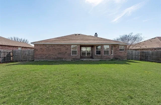 Expansive backyard featuring a manicured lawn, brick exterior, multiple windows, and a wood privacy fence