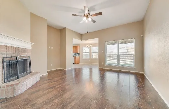 Vaulted ceiling with a ceiling fan, brick-clad fireplace with a white mantel, wood-finish flooring, and large windows with blinds