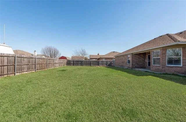 Expansive backyard featuring a manicured lawn, full wood privacy fencing, a covered patio, and a brick exterior
