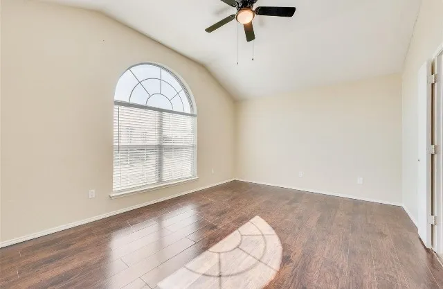 Vaulted ceiling with a ceiling fan, arched window with horizontal blinds, wood-finish flooring, and light-toned walls