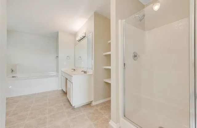 Tiled flooring, dual vanity with undermount sinks, built-in shelving, shower enclosure, and a soaking tub