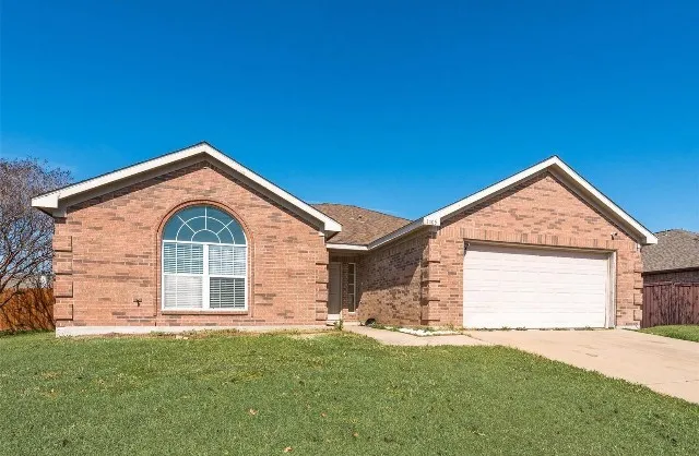 Brick exterior with arched window detail and white trim accents, two-car garage with white overhead door, and manicured front lawn with mature landscaping