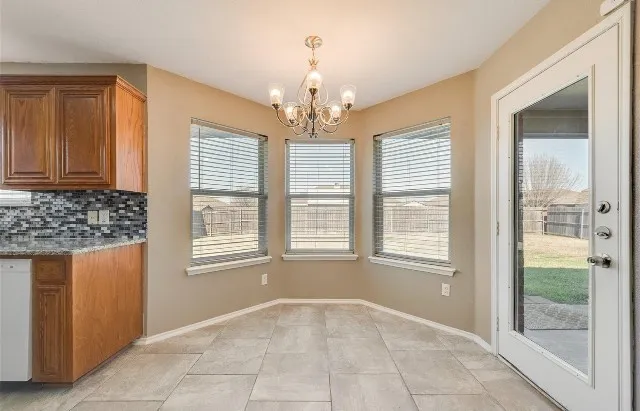 Bay window with three panes, tile flooring, glass-paneled door, hanging chandelier, and wood-finish cabinetry