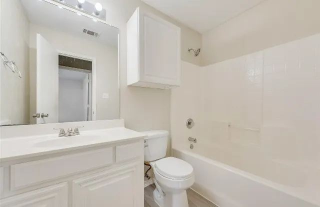 White vanity with integrated sink, chrome faucet, wall-mounted mirror, and overhead cabinet