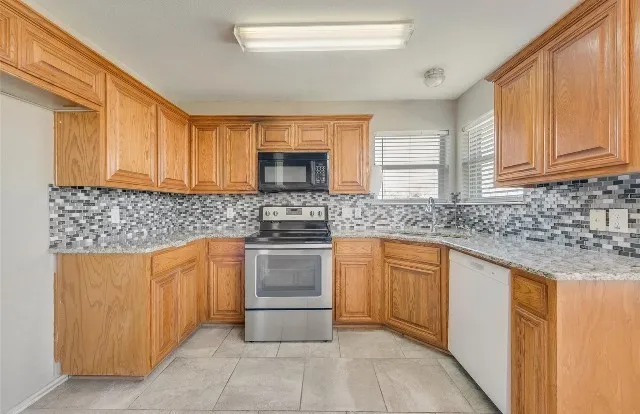 U-shaped kitchen with wood cabinetry, tile flooring, a mosaic tile backsplash, and light-toned countertops