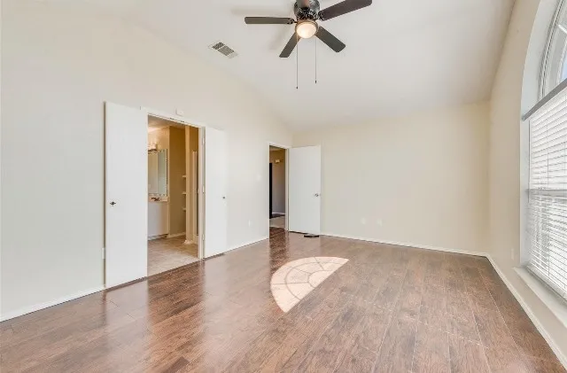 Vaulted ceiling, wood-finish flooring, arched window with blinds, ceiling fan, and double doors