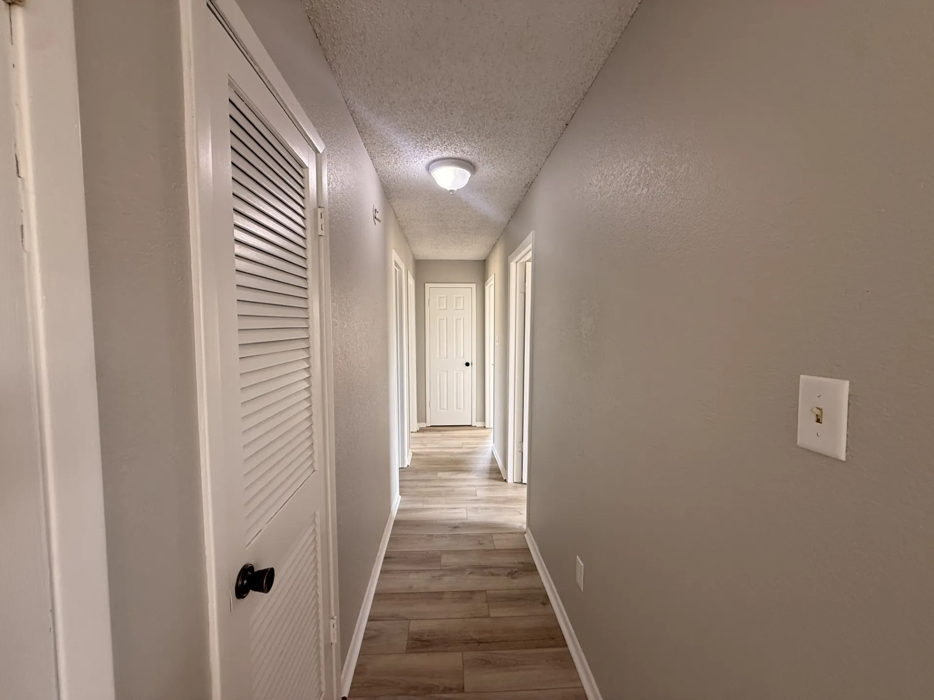 Hallway featuring wood-finish flooring, neutral wall paint, and white paneled doors