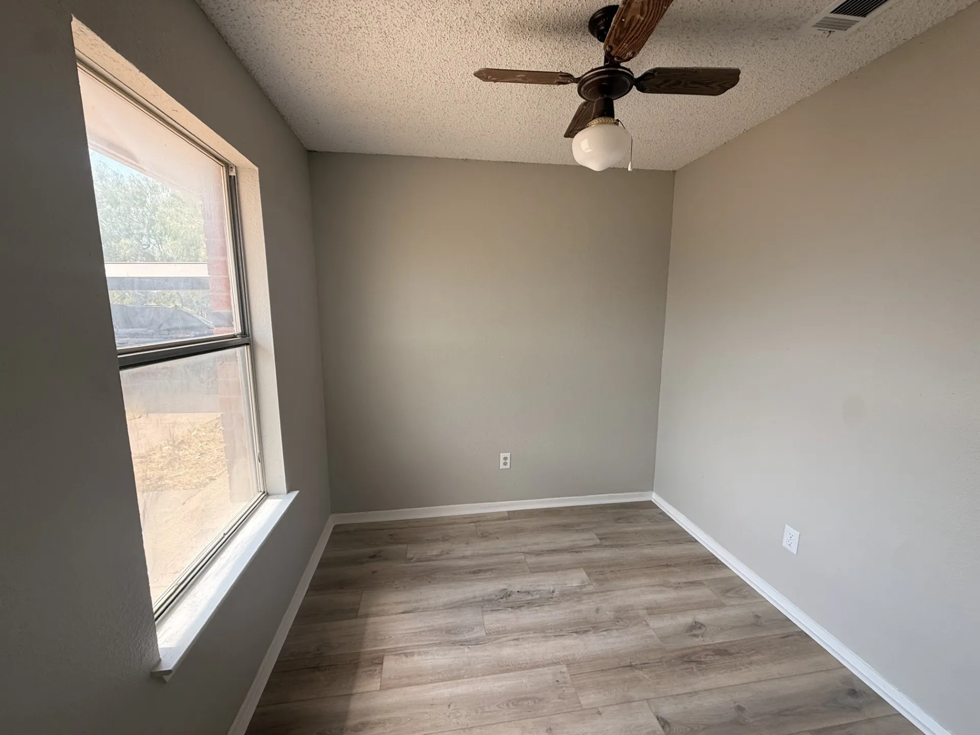 Wood-finish flooring, neutral wall tones, ceiling fan with light fixture, and window with trim