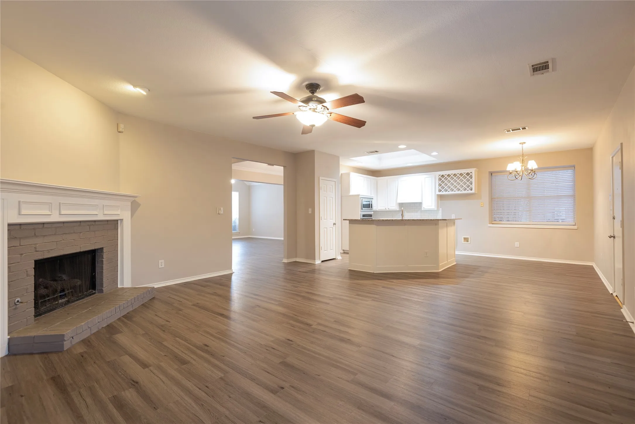 Unfurnished living room with a fireplace, ceiling fan with notable chandelier, and dark wood-type flooring