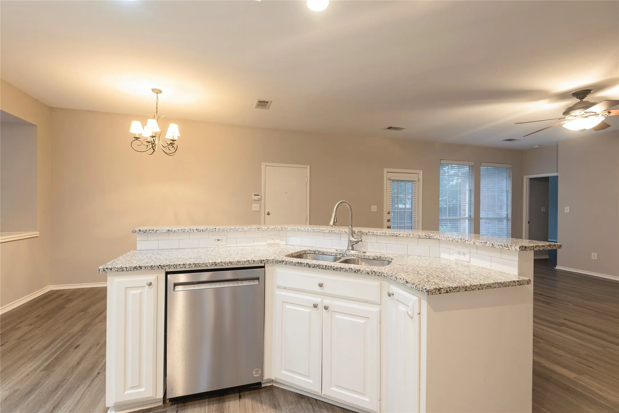 Kitchen with stainless steel dishwasher, a kitchen island with sink, sink, decorative light fixtures, and white cabinets