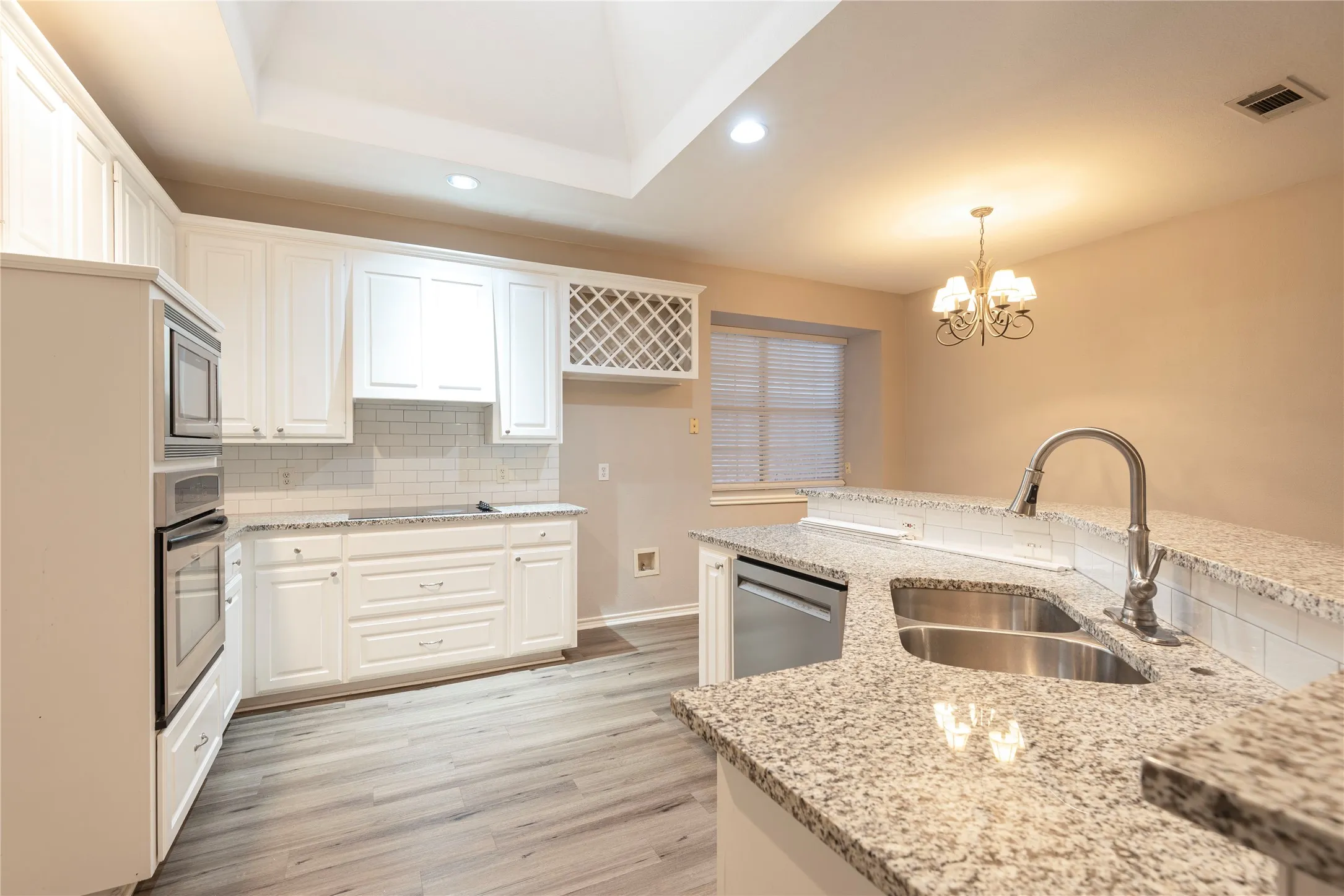 Kitchen with pendant lighting, white cabinets, sink, light stone counters, and stainless steel appliances