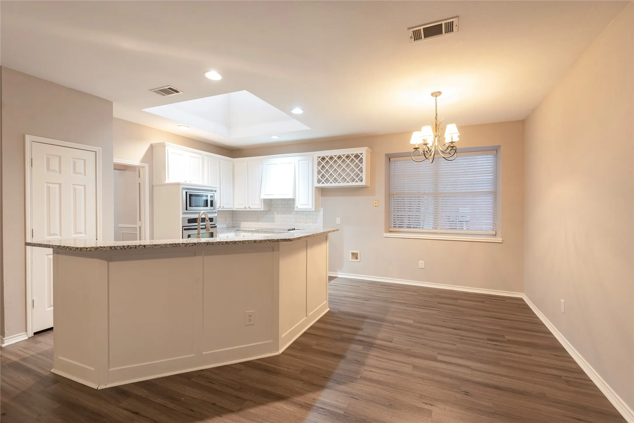Kitchen featuring light stone countertops, decorative light fixtures, white cabinetry, and a kitchen island with sink