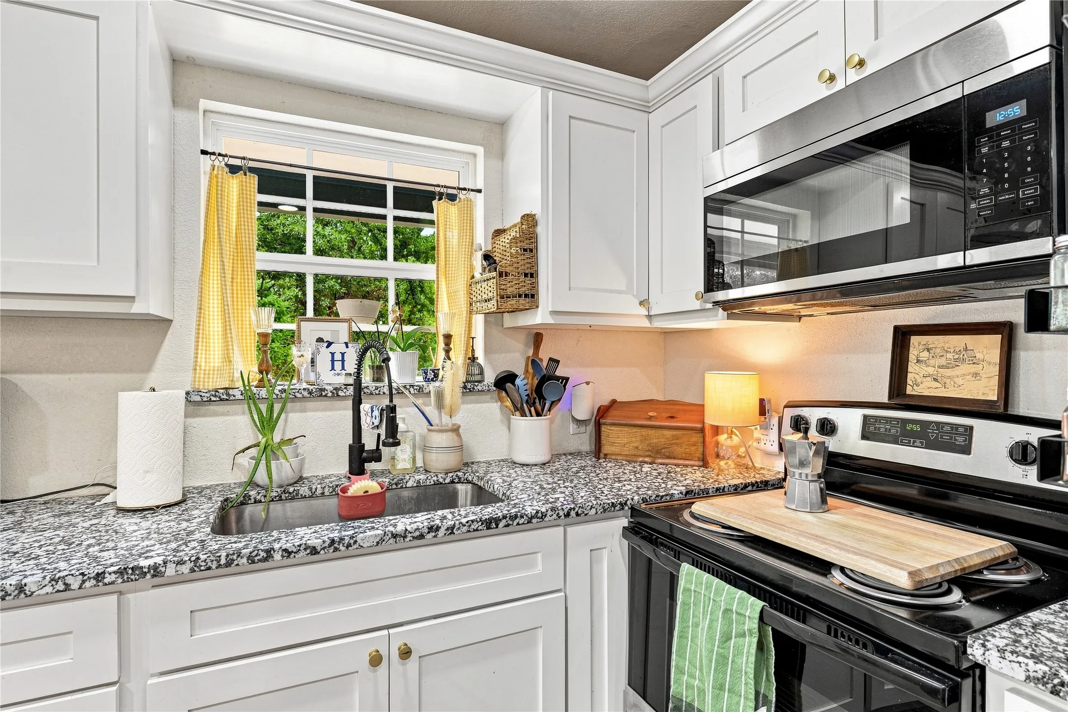 White shaker-style cabinetry with gold-tone hardware, speckled countertops, stainless steel sink with a matte black faucet, built-in microwave, and electric range