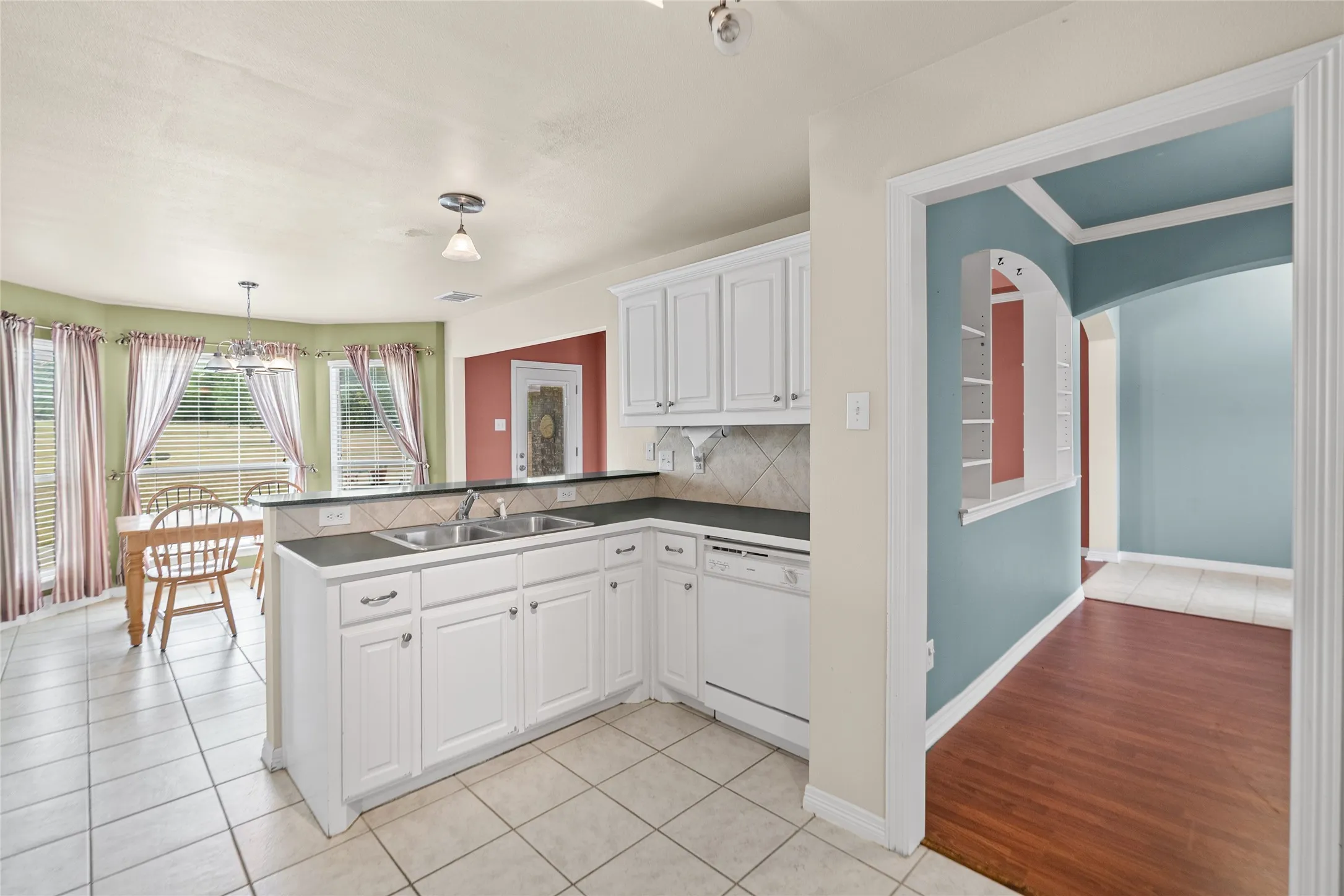 Kitchen featuring white cabinetry, dual basin sink, integrated dishwasher, and tile flooring