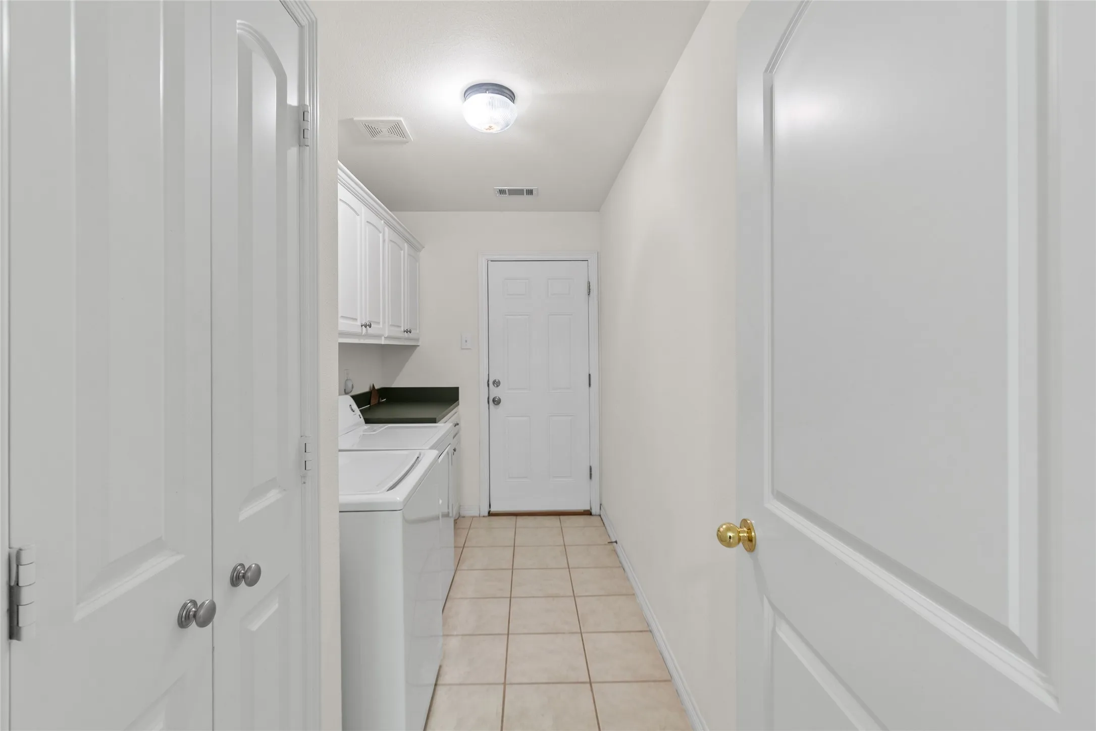 Laundry area featuring white cabinetry, dark countertops, and tile flooring