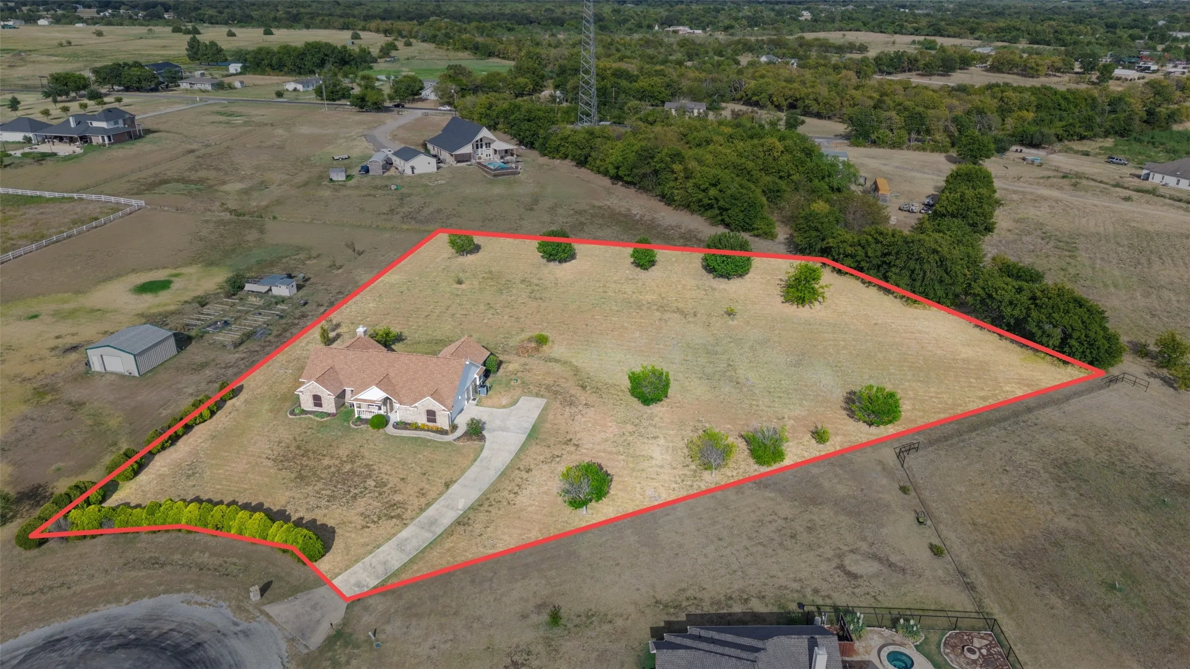 Expansive lot featuring a single-story residence, a winding paved driveway, and established perimeter landscaping