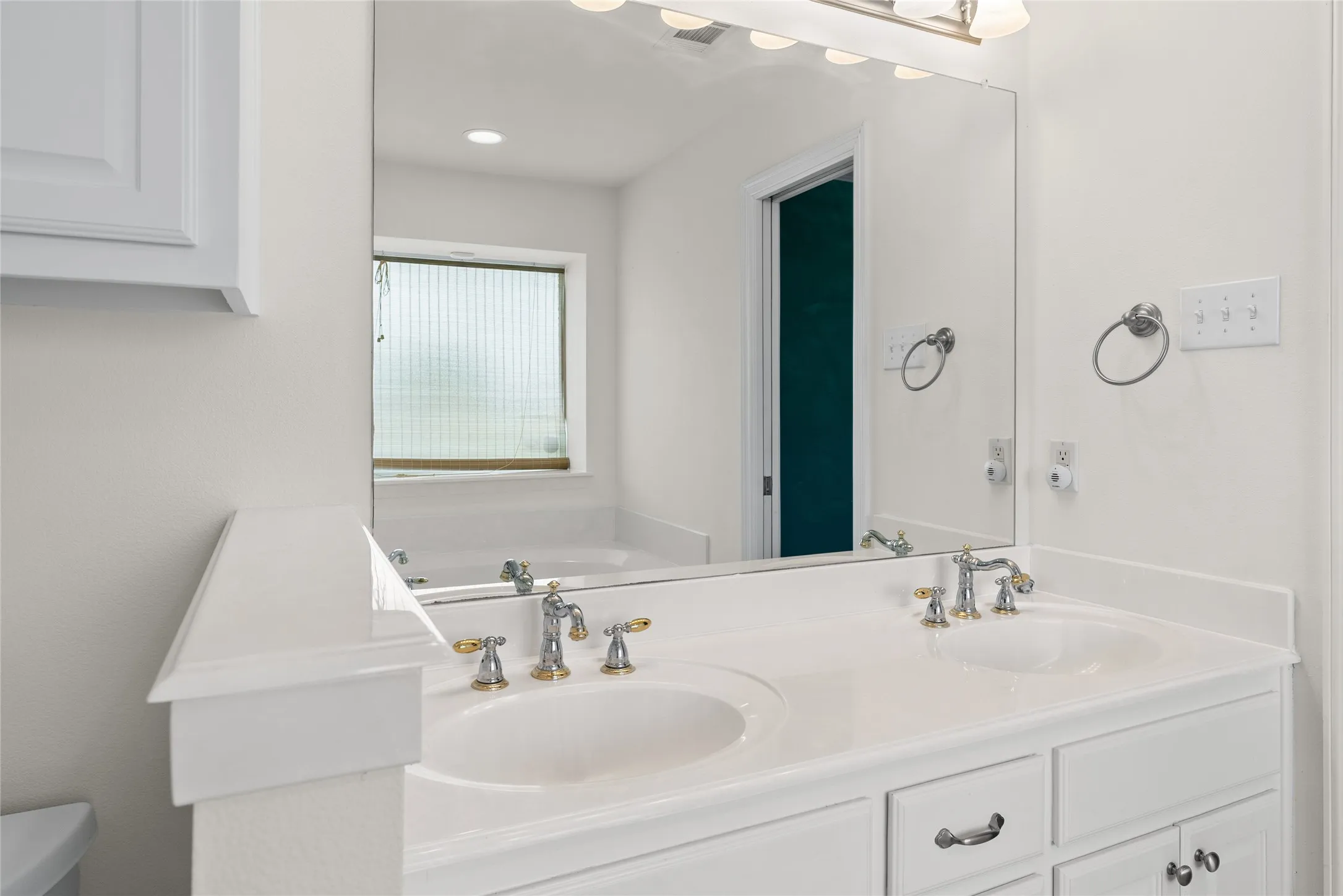 Dual undermount sinks with chrome and gold-tone fixtures, extensive vanity countertop, and under-sink cabinetry