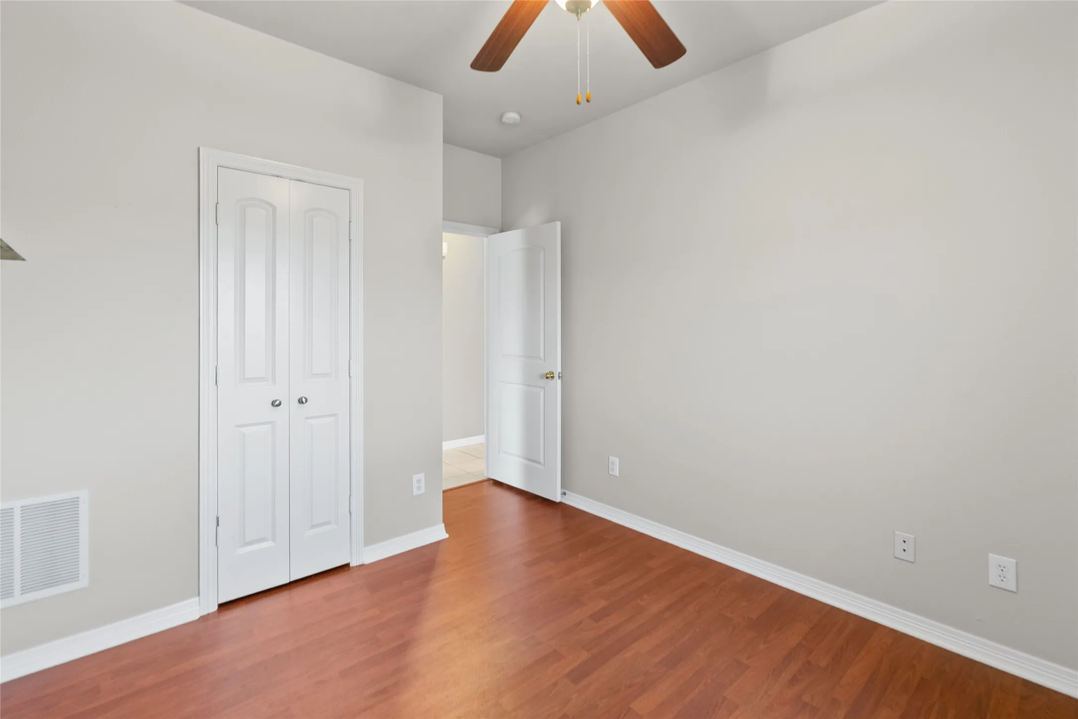 Warm wood-finish flooring, white bi-fold closet doors, and a ceiling fan with integrated lighting