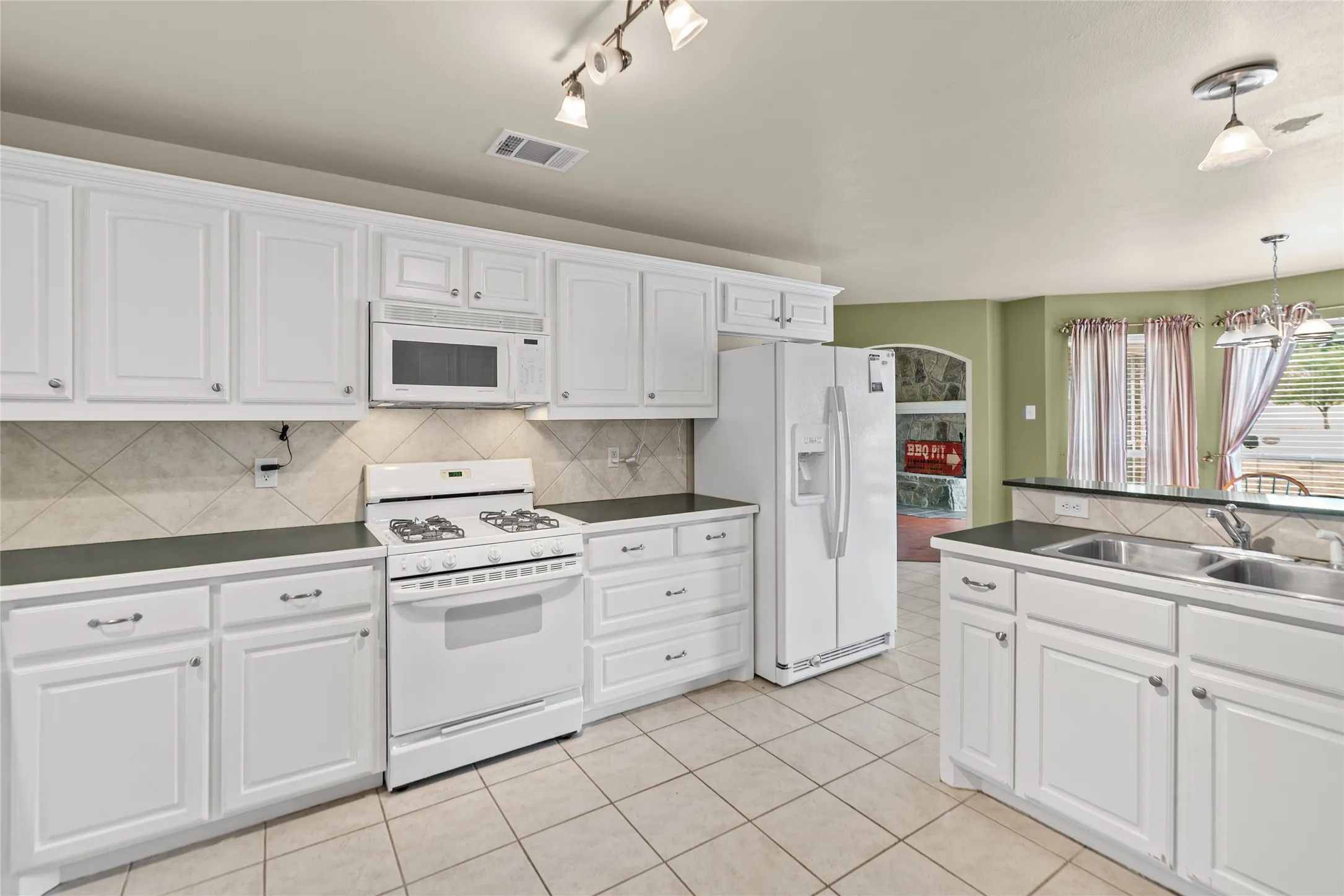 White cabinetry, tile flooring, built-in microwave, dual basin sink, and an integrated refrigerator
