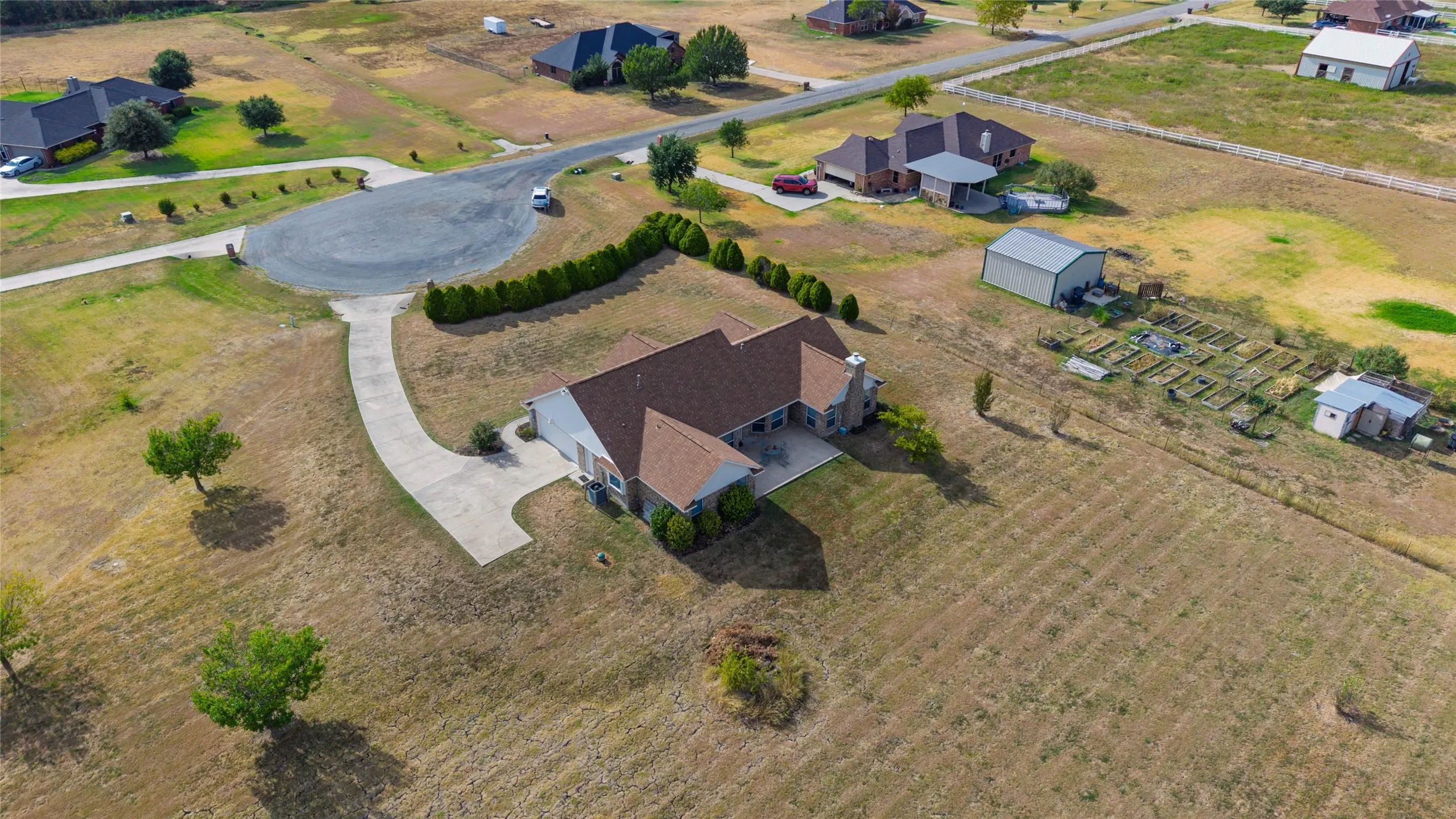 Expansive property featuring a single-story residence with a concrete drive, detached metal shed, and structured garden beds