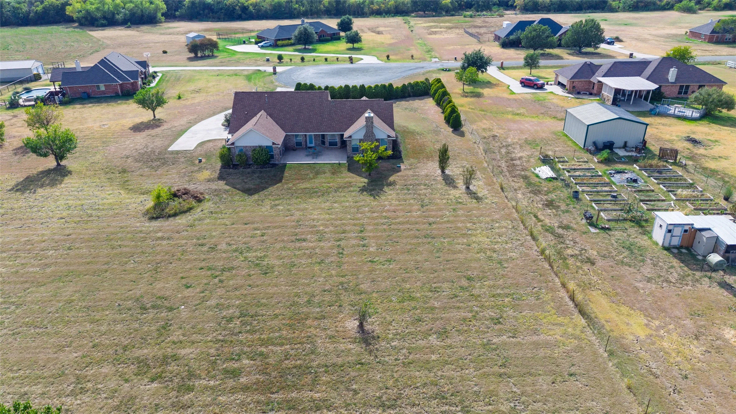 Ranch-style residence featuring a brick and siding exterior, a front porch with columns, a curved concrete driveway, and a detached metal building