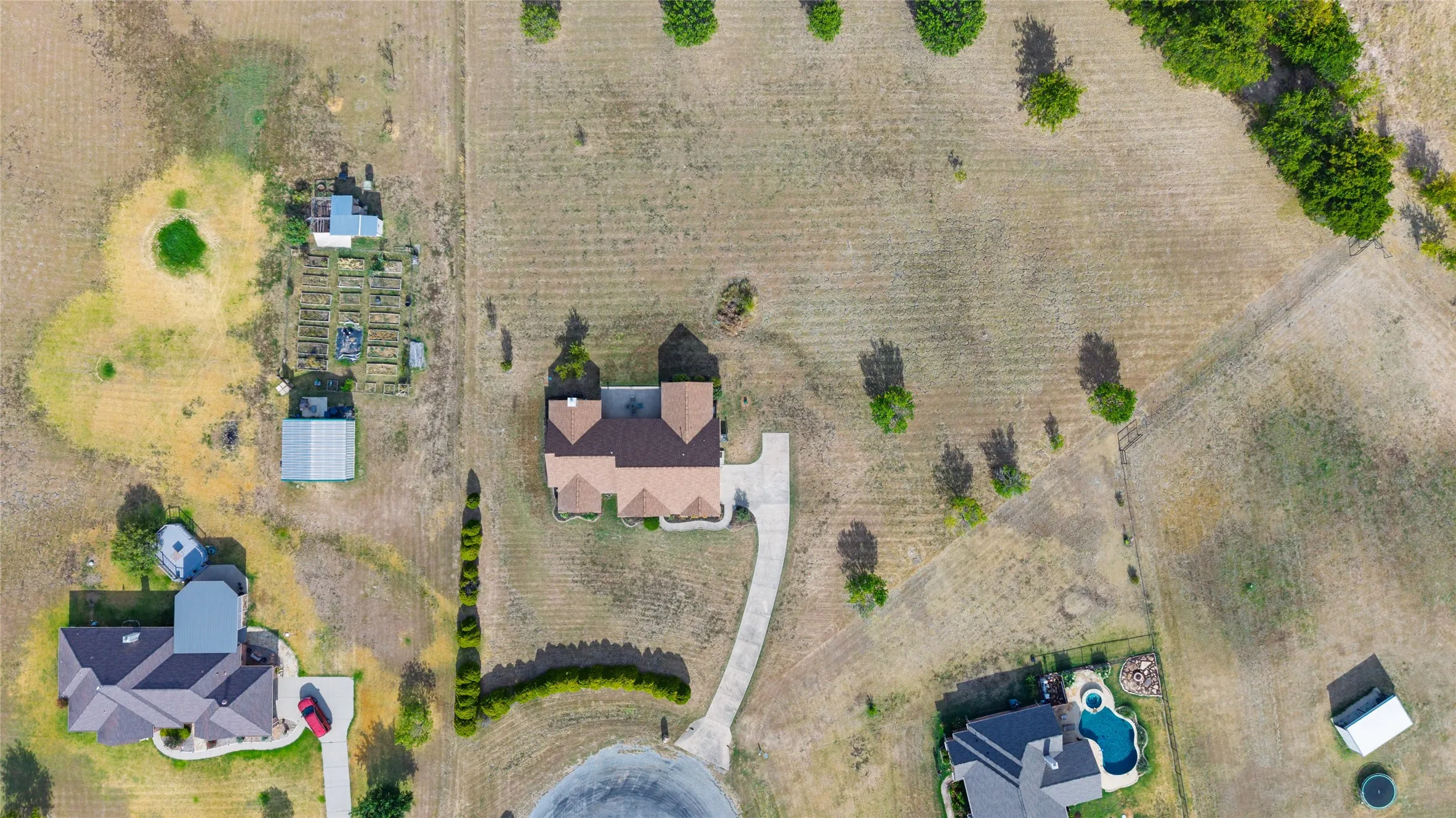 Expansive property featuring a cul-de-sac location, paved driveway, multiple outbuildings, and cultivated garden beds