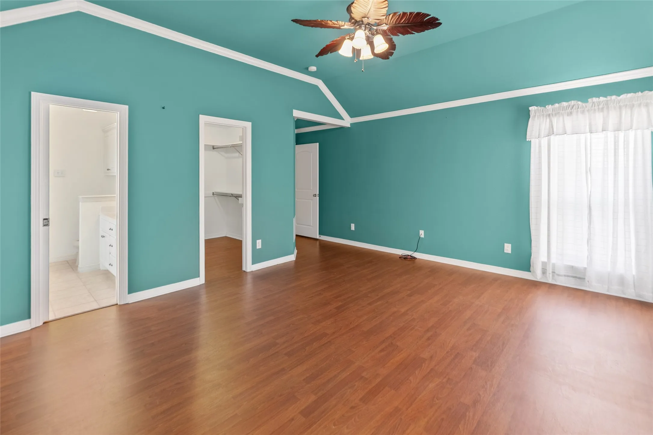 Vaulted ceiling with a ceiling fan, wood-finish flooring, two white doors, and a window with white trim