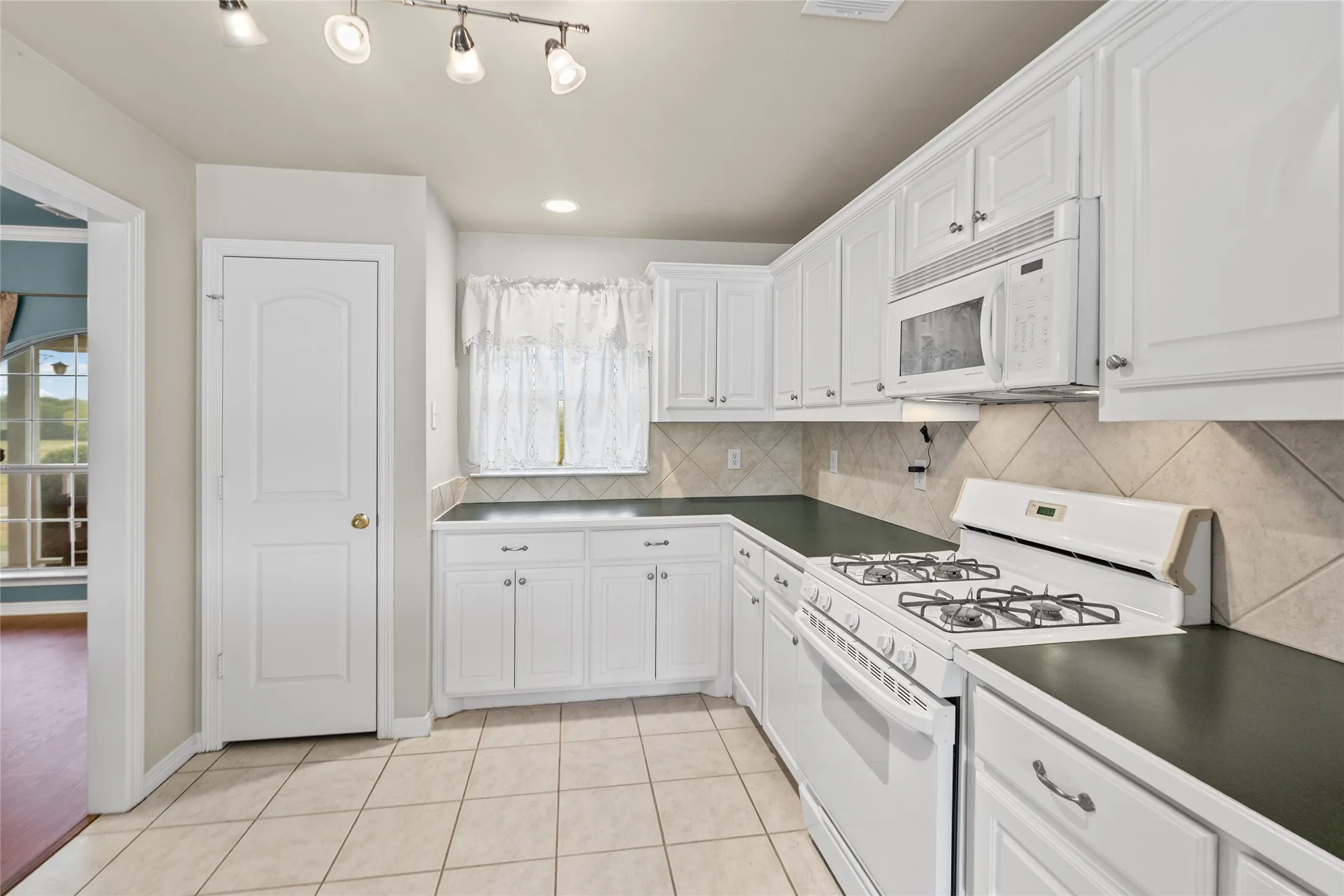 Kitchen featuring white cabinetry, dark countertops, a built-in microwave, a gas range, and tile flooring