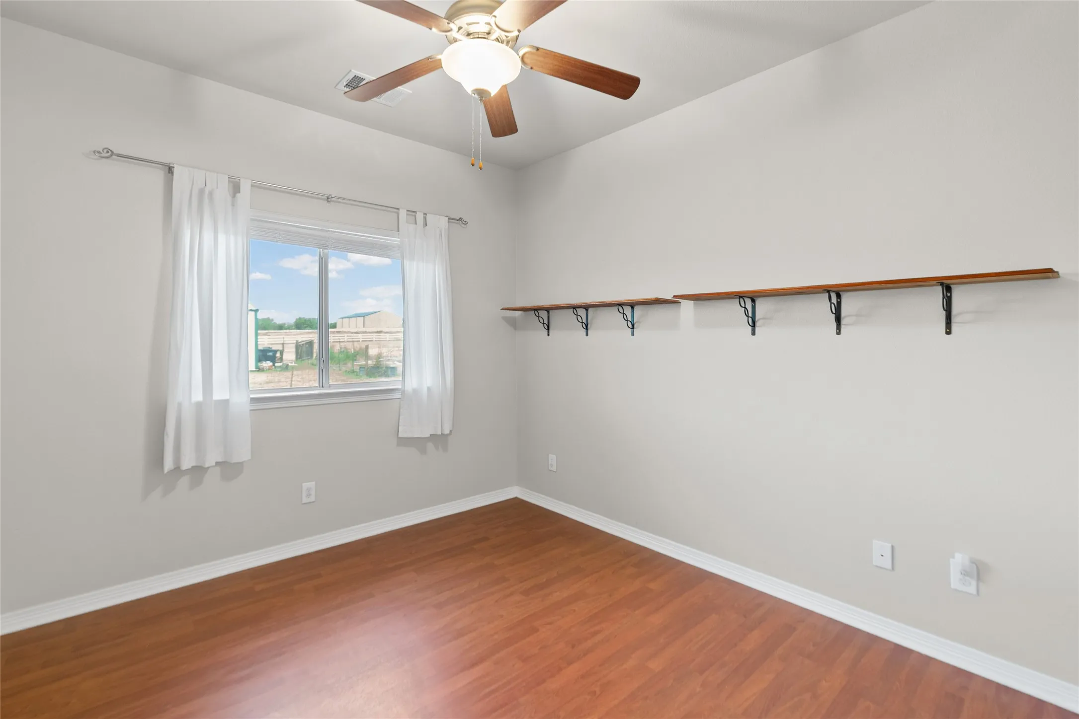 Wood-finish flooring, ceiling fan, natural light from the window, and built-in wall shelving