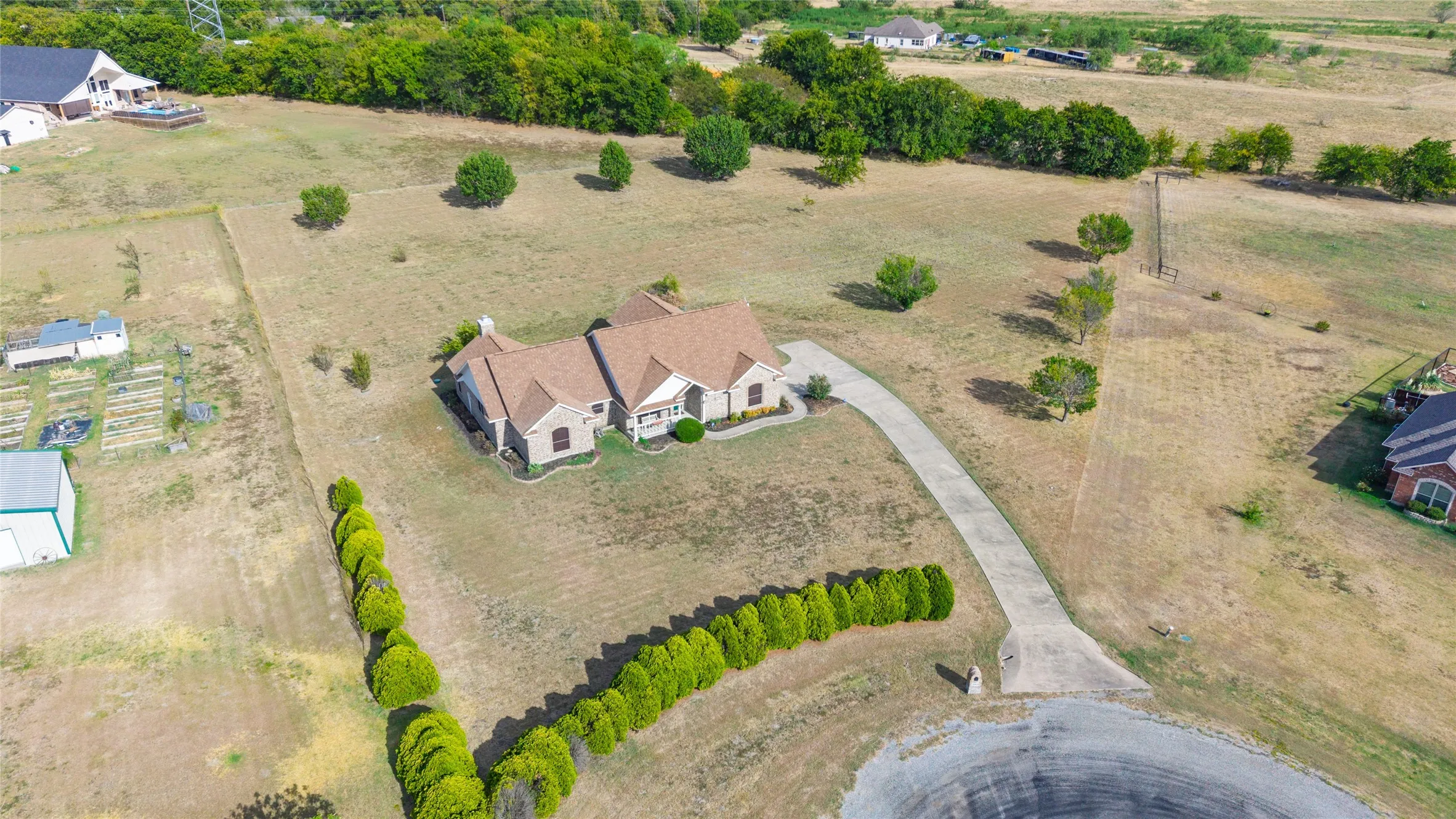 Expansive property featuring a stone and brick exterior, a multi-gabled roofline, a curved concrete driveway, and established perimeter hedging
