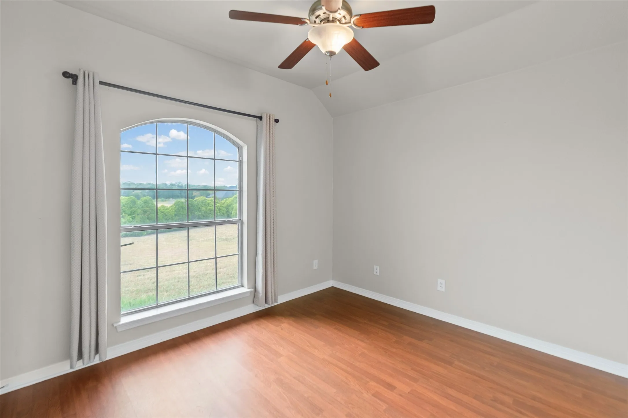 Arched window with grid panes, wood-finish flooring, light neutral wall paint, and a ceiling fan with integrated lighting