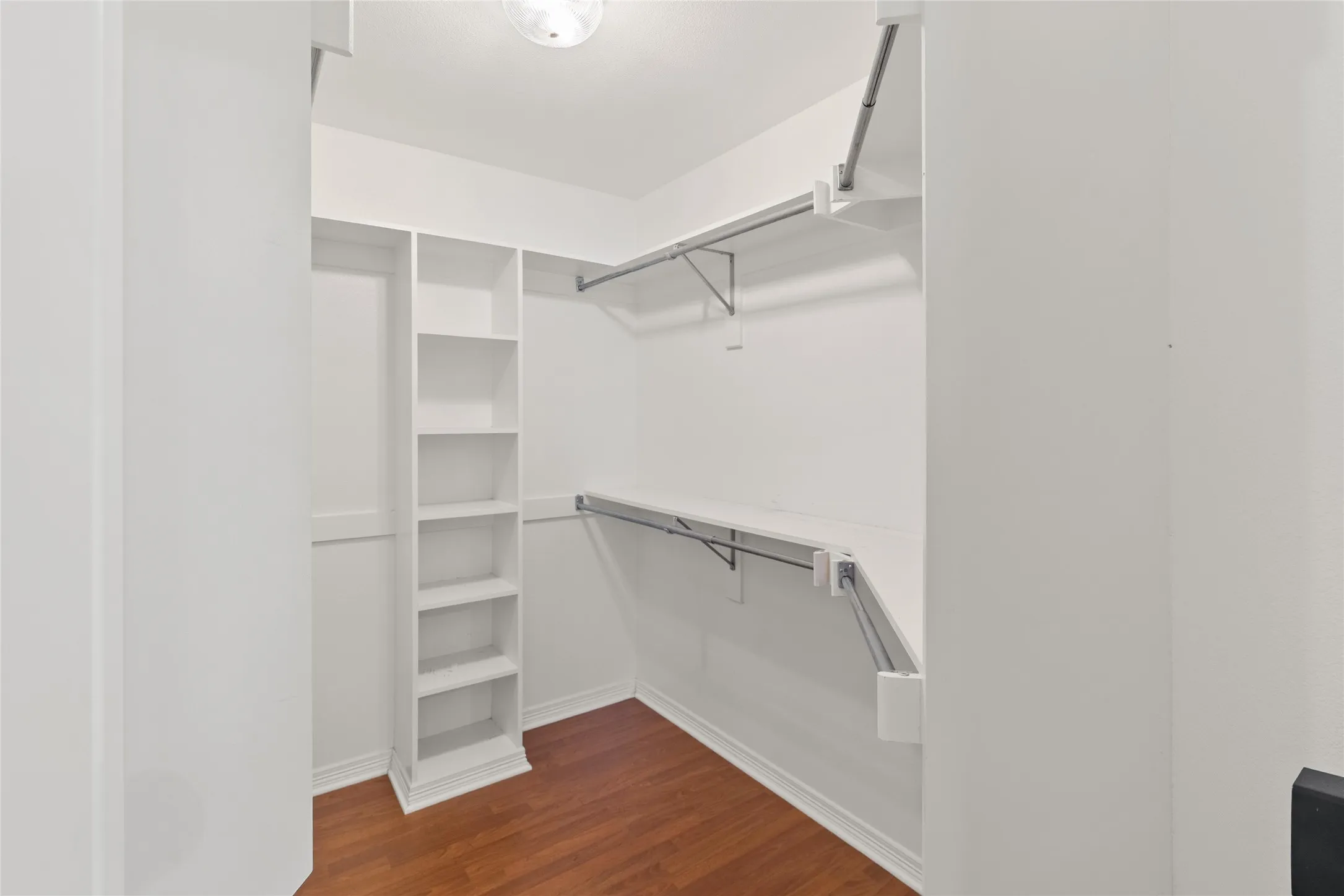 Walk-in closet with integrated shelving, multiple hanging rods, and wood-finish flooring