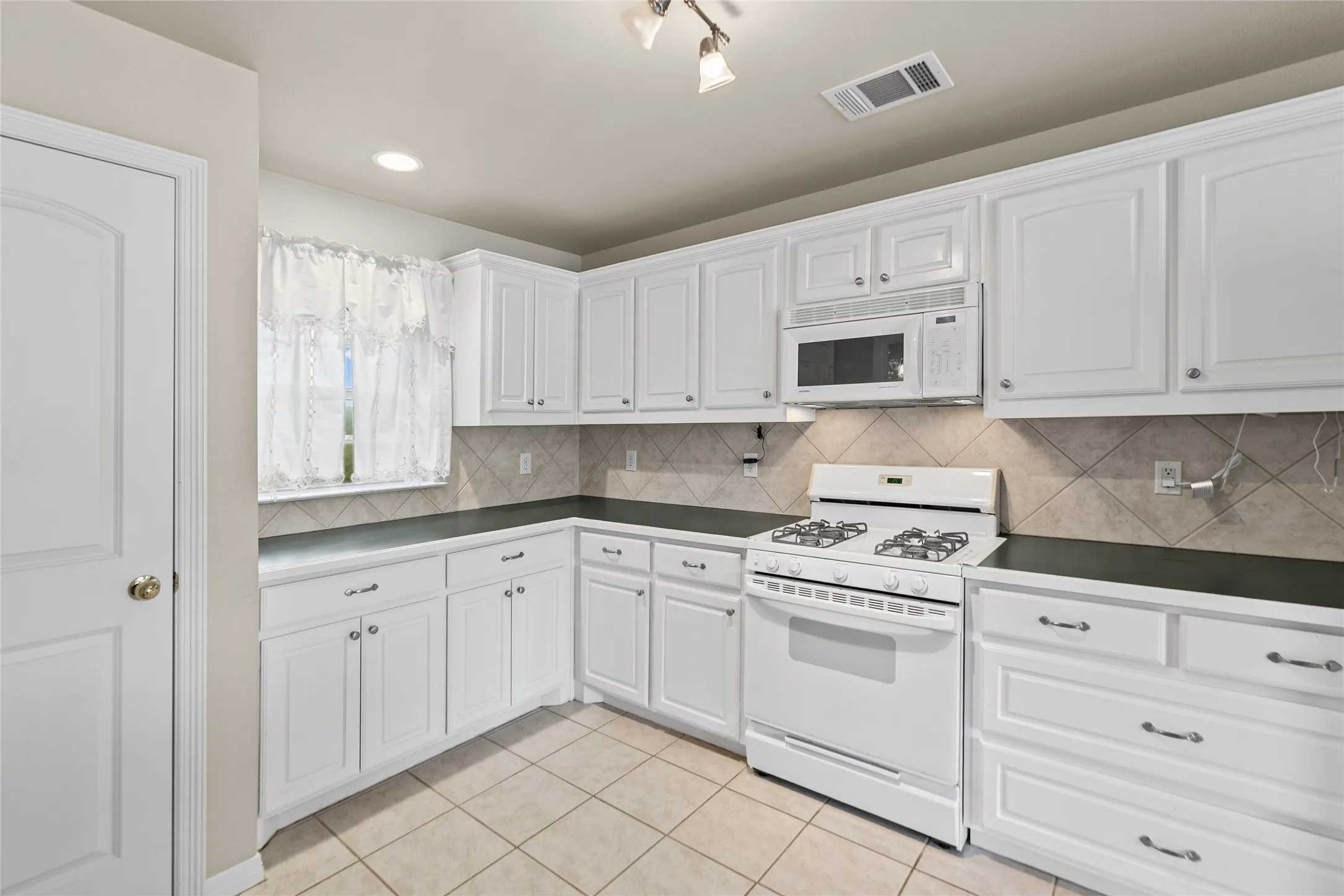 White cabinetry with brushed nickel hardware, built-in microwave, gas range, tile backsplash, and tile flooring