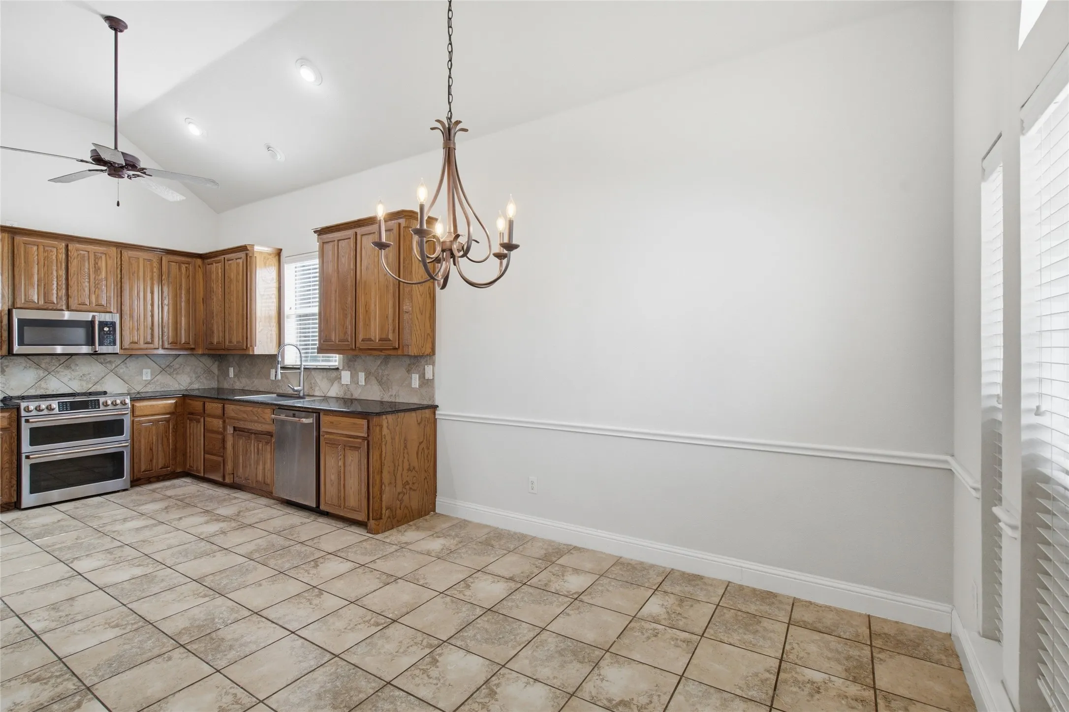 Vaulted ceiling kitchen featuring wood cabinetry, stainless steel appliances, and a tile backsplash