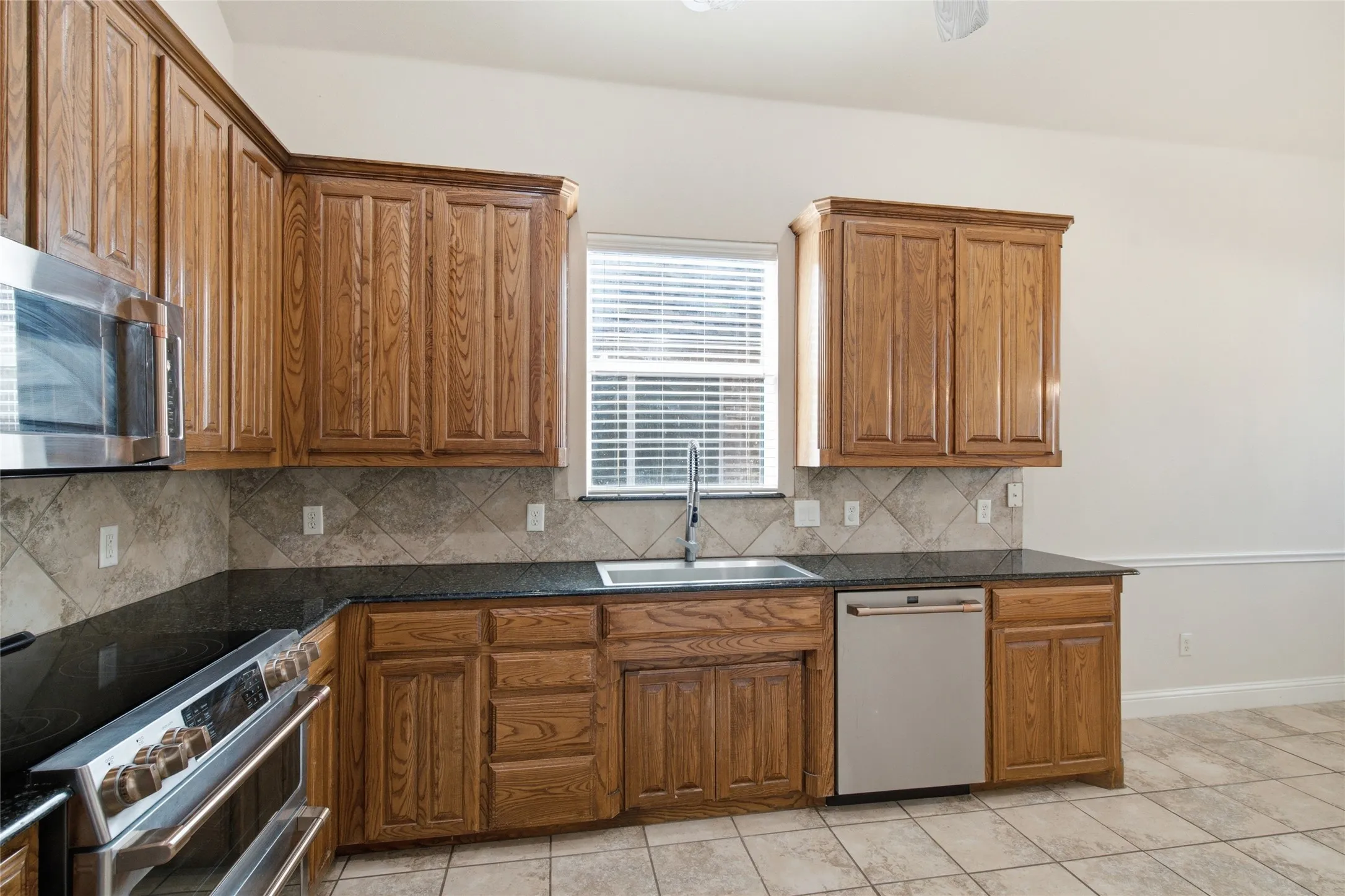 Kitchen featuring wood-finish cabinetry, dark countertops, a stainless steel sink, and stainless steel appliances including an oven, microwave, and dishwasher