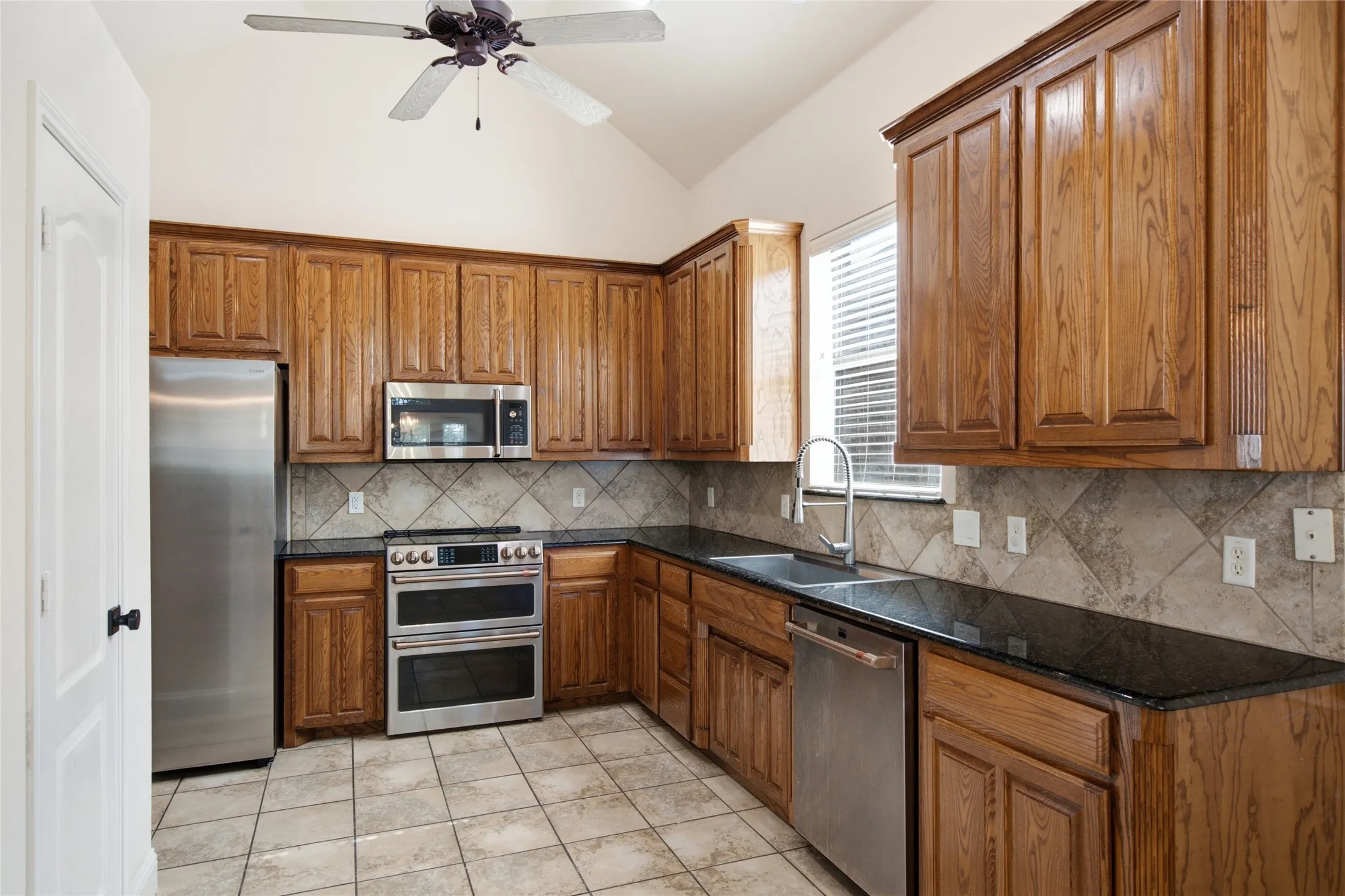 Kitchen featuring wood cabinetry, dark countertops, a tile backsplash, and stainless steel appliances