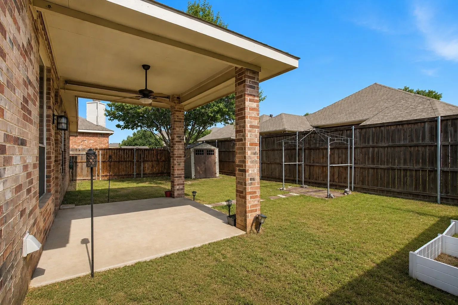 Covered patio with a ceiling fan, brick support columns, and an outdoor wall-mounted light fixture