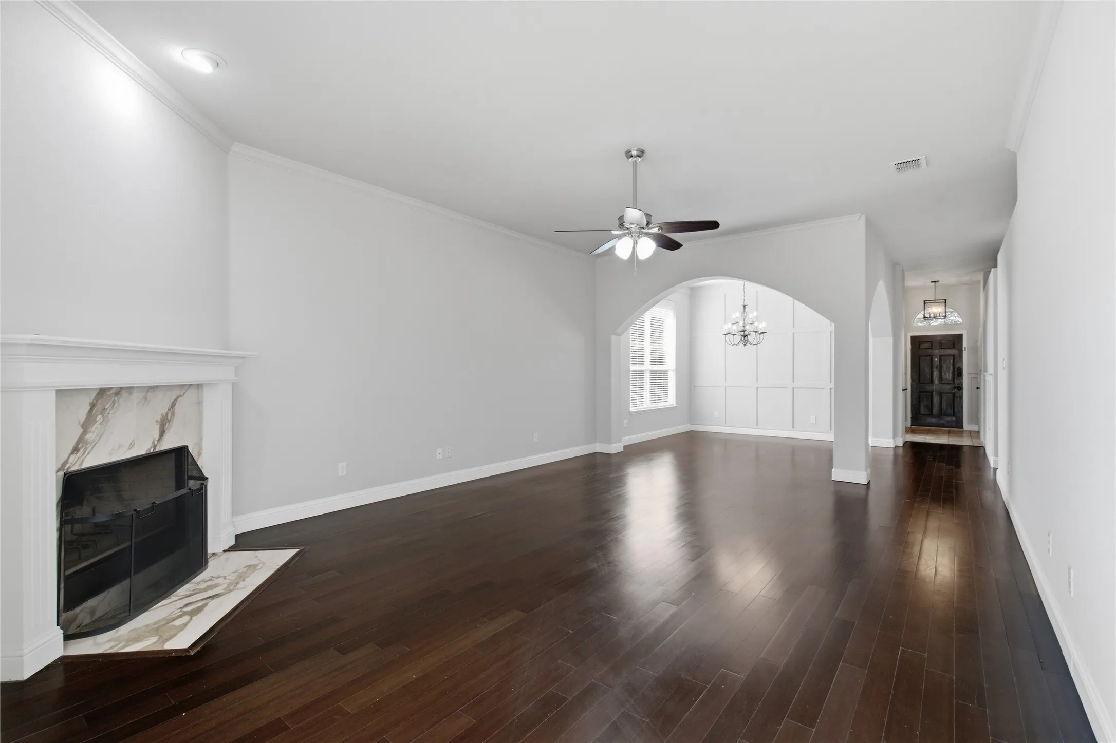 Hardwood flooring, fireplace with marble-look surround, arched doorways, crown molding, and recessed lighting
