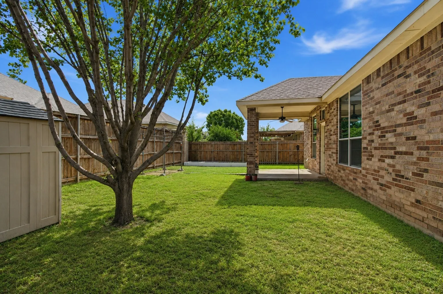 Expansive backyard with a covered patio, brick columns, and a ceiling fan