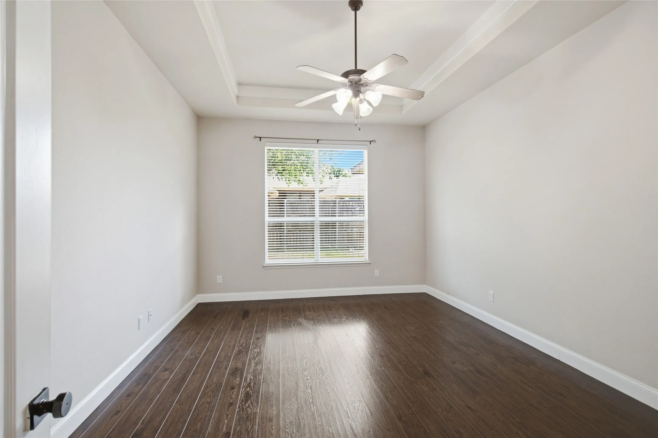 Wood-finish flooring with white baseboards, a single window with blinds, and a ceiling fan with light fixture