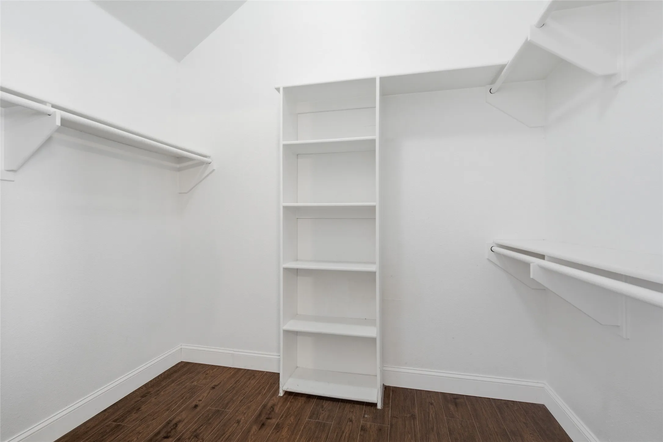 Spacious closet featuring wood-finish flooring, built-in shelving, and multiple clothing rods