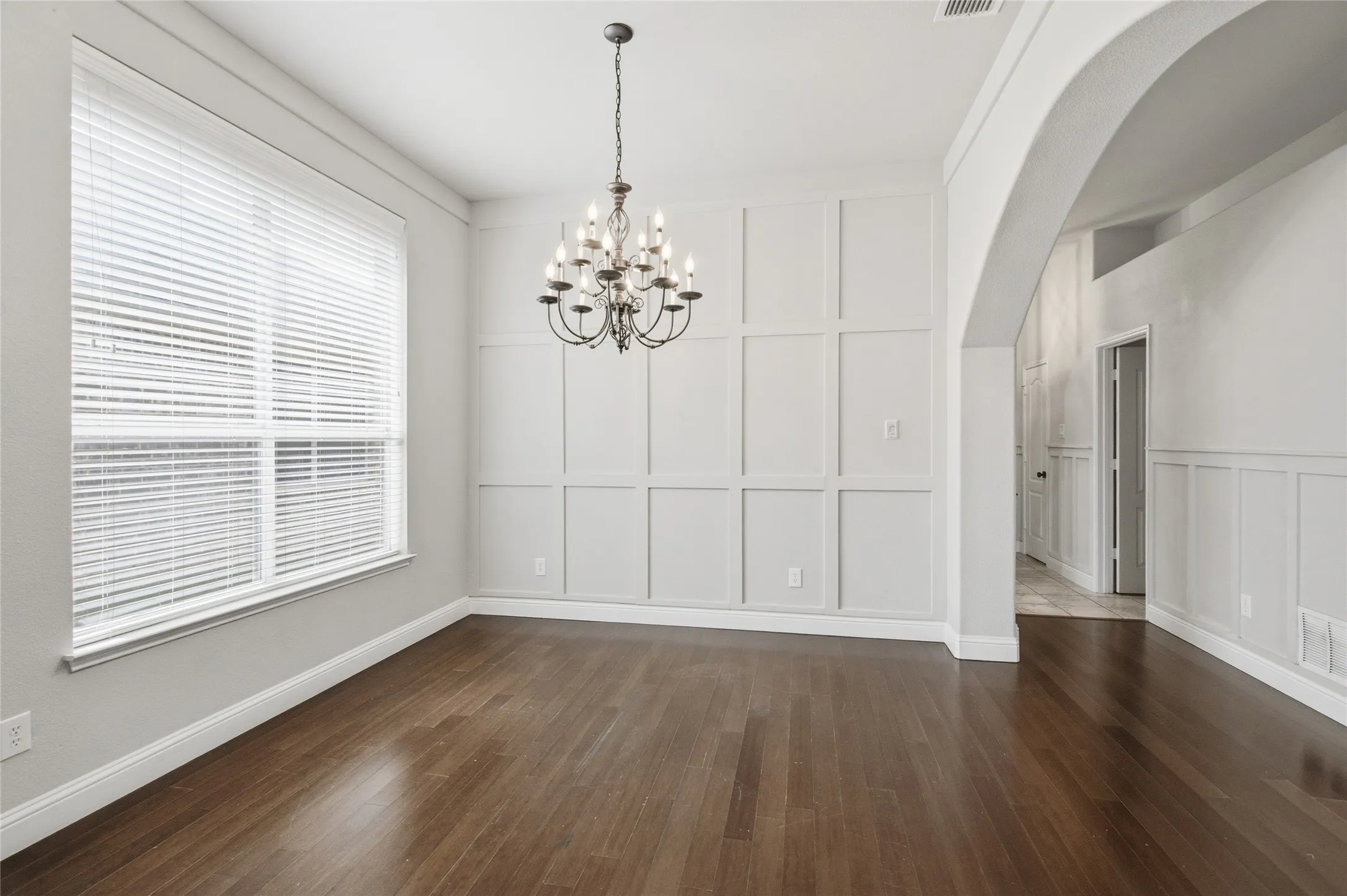 Dark wood-finish flooring, a decorative chandelier, and wainscoting with wall paneling