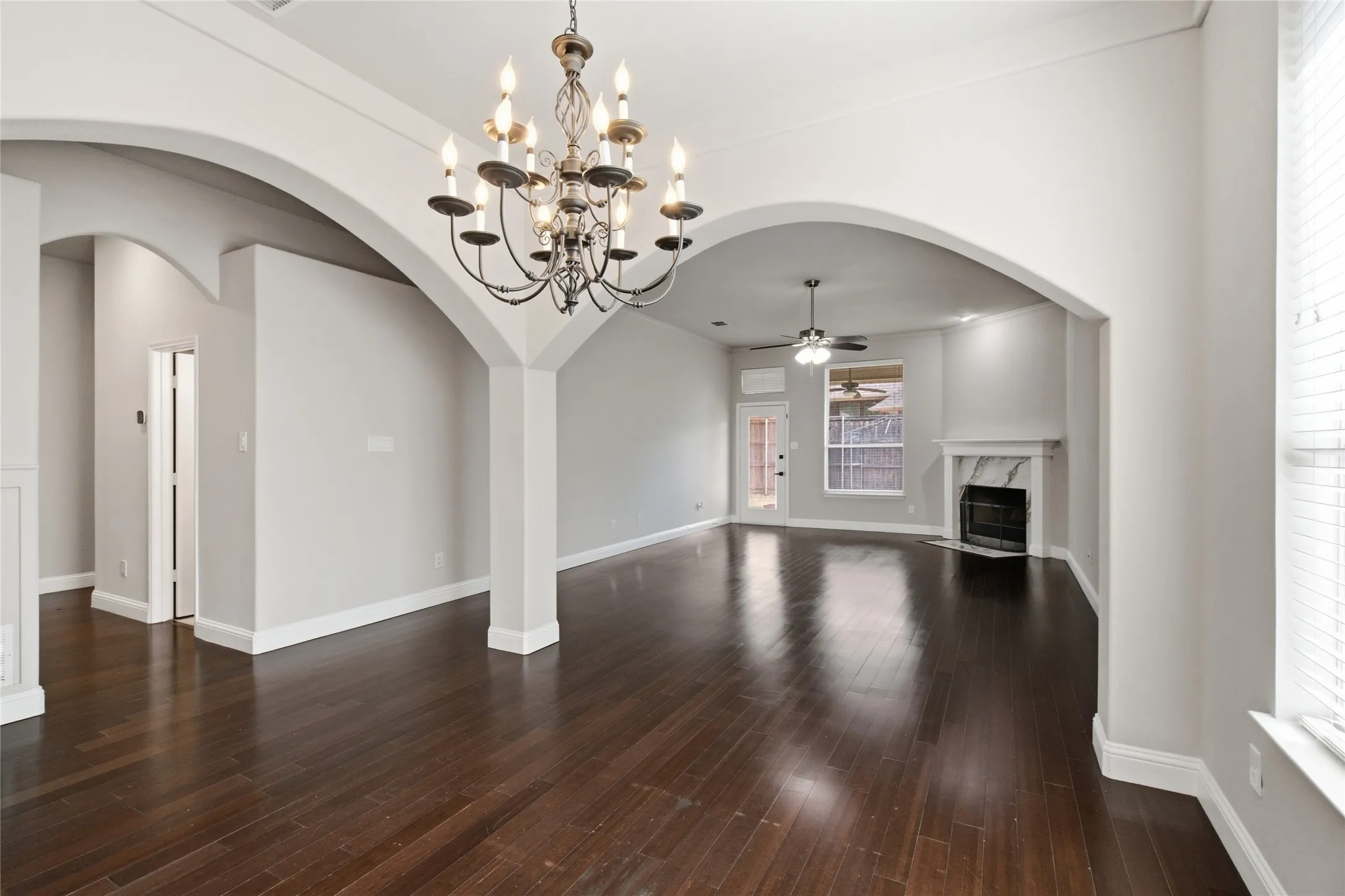 Dark wood-finish flooring, arched doorways, a decorative chandelier, a fireplace with a stone surround, and a ceiling fan