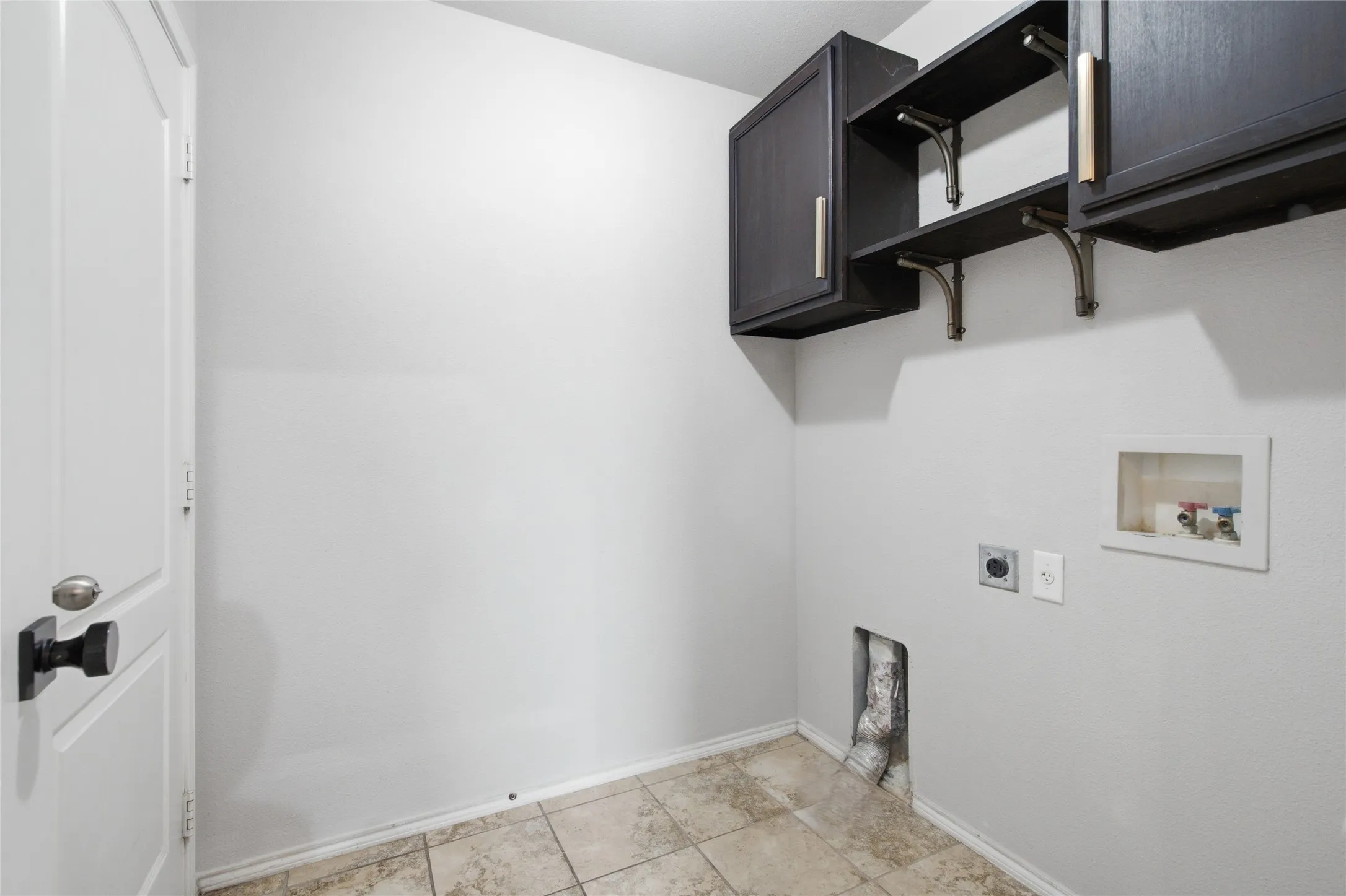 Wall-mounted dark cabinetry with brass-tone hardware, open shelving with decorative brackets, tile flooring, and a paneled white door with black hardware