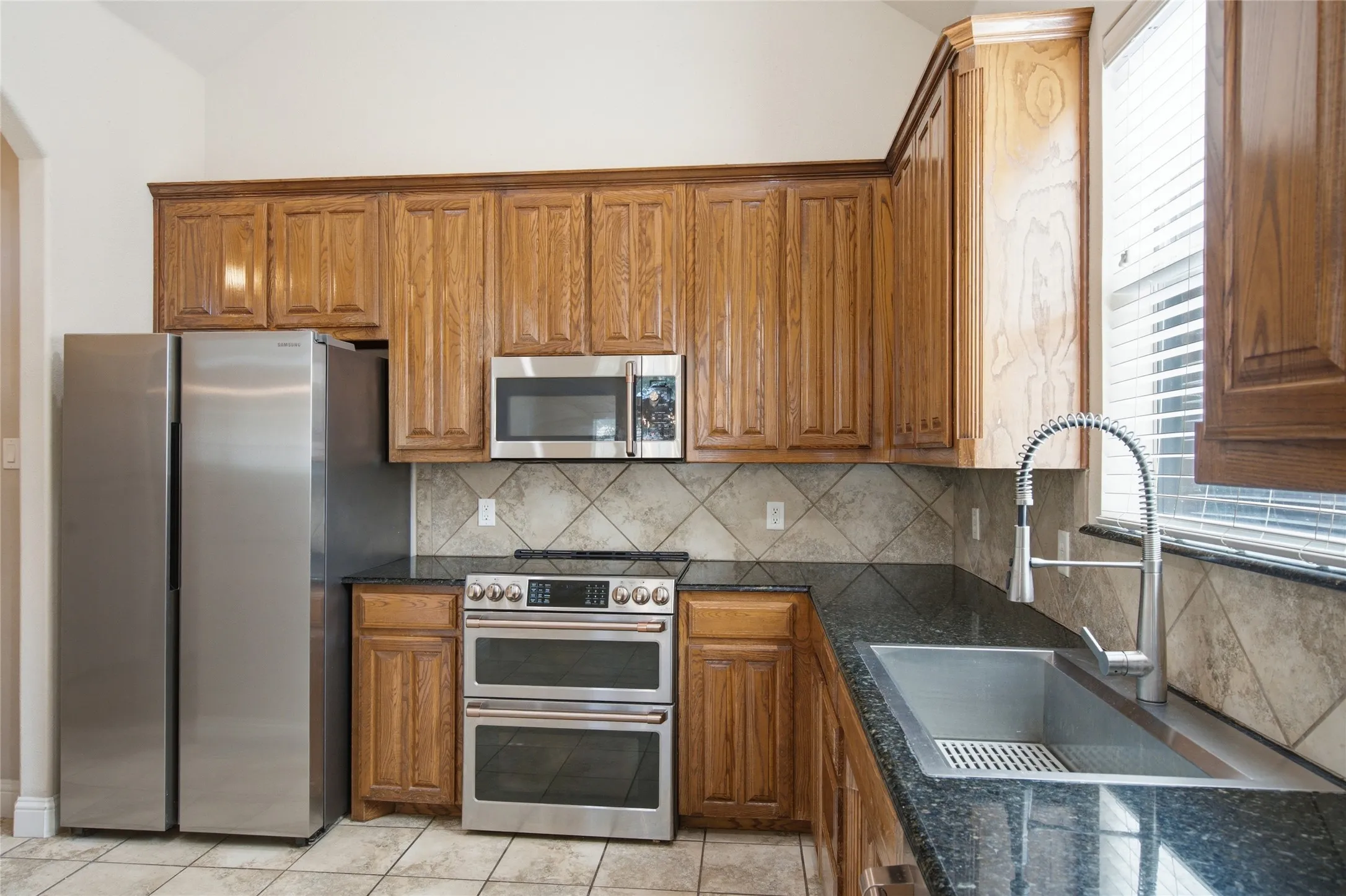 Kitchen featuring wood-finish cabinetry, stainless steel appliances, dark stone countertops, and tile flooring